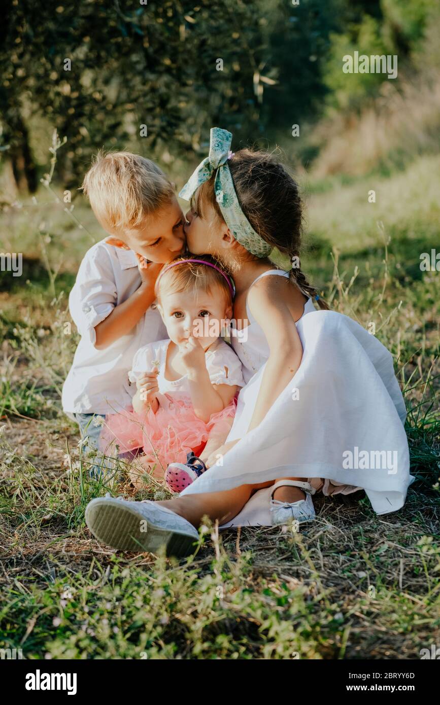 Portrait of two girls and a boy sitting in a sunny garden. Stock Photo