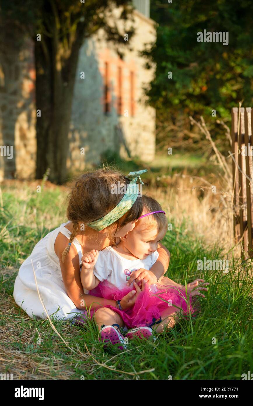 Portrait of two girls sitting in a sunny garden. Stock Photo