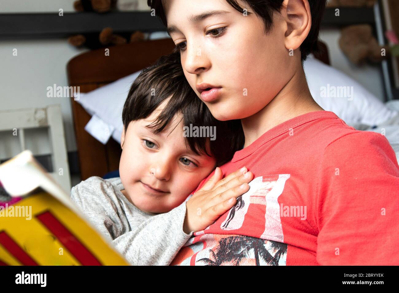 Two brothers sitting on bed, cuddling and reading book. Stock Photo