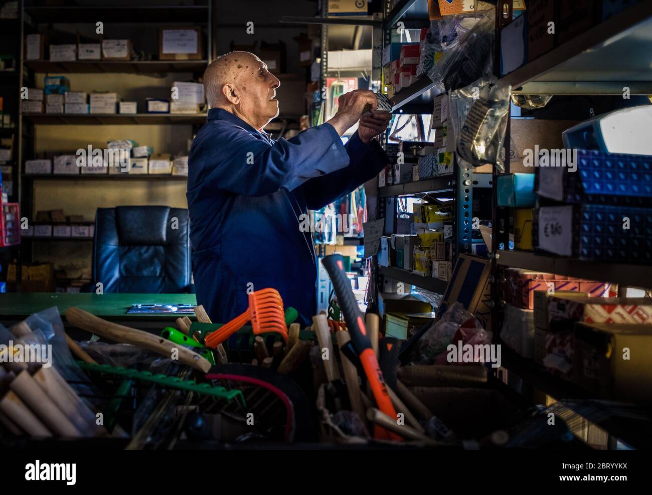 https://c8.alamy.com/comp/2BRYYKX/an-ironmonger-elderly-man-in-a-boiler-suit-searching-through-shelves-stacked-with-useful-household-items-and-tools-2BRYYKX.jpg