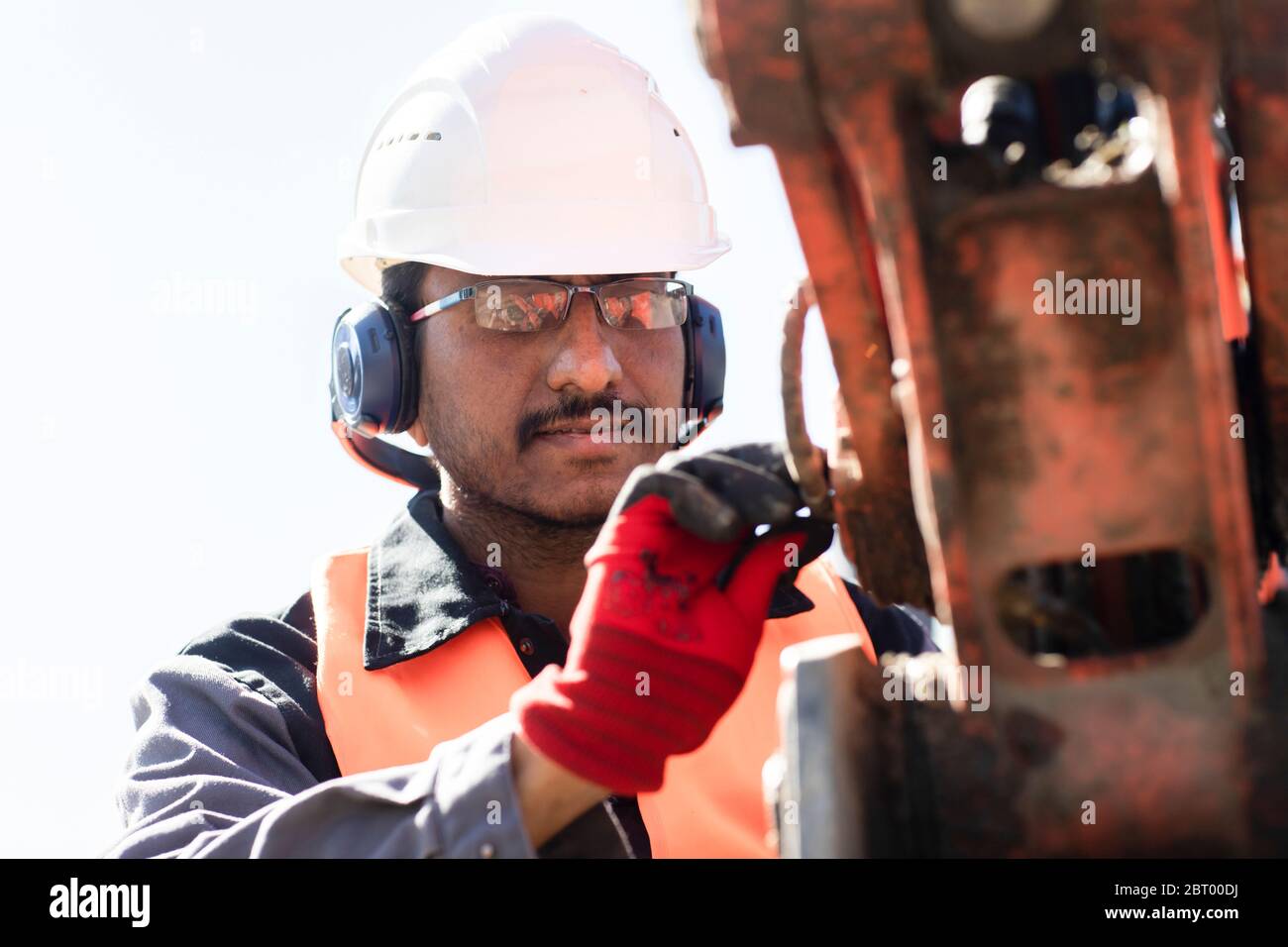 Male engineer wearing hardhat and ear protectors working on construction site. Stock Photo