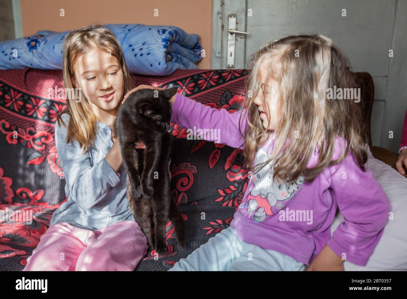 Little girls playing with black cat in the rural home. Stock Photo