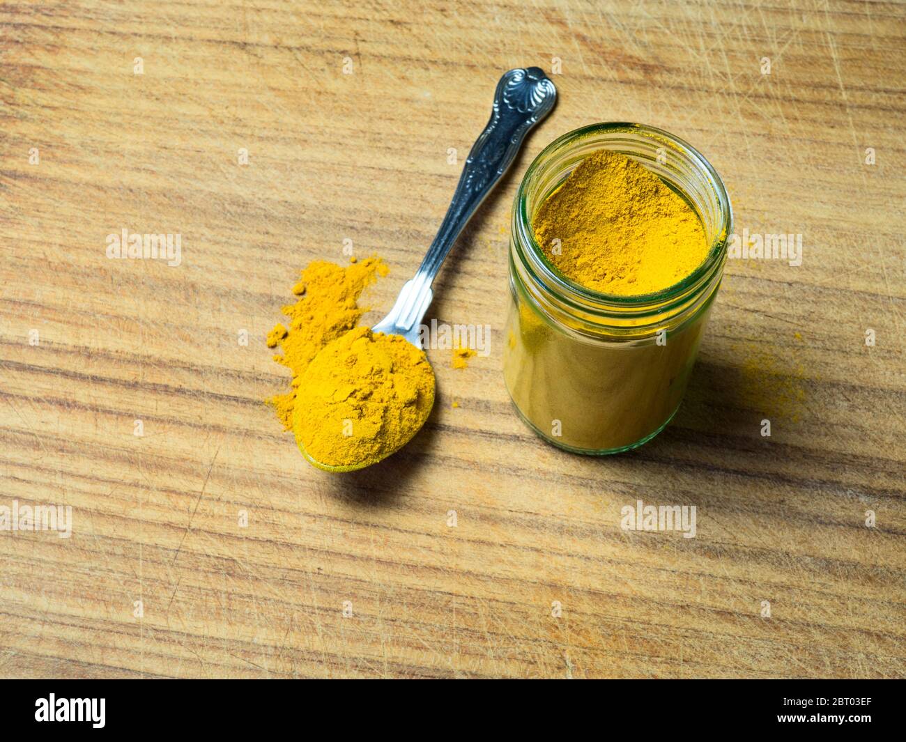 A glass jar of turmeric with a teaspoonful of turmeric on a wooden board Stock Photo