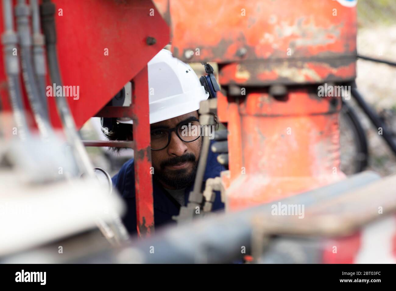 Bearded man wearing eyeglasses and white hard hat working on construction site. Stock Photo