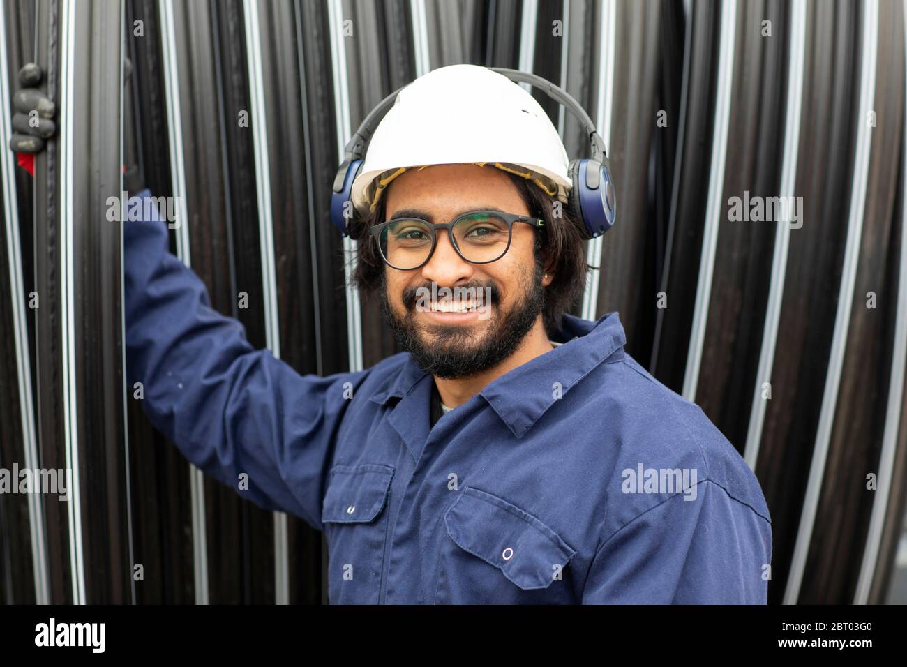 Bearded man wearing eyeglasses and white hard hat working on construction site. Stock Photo