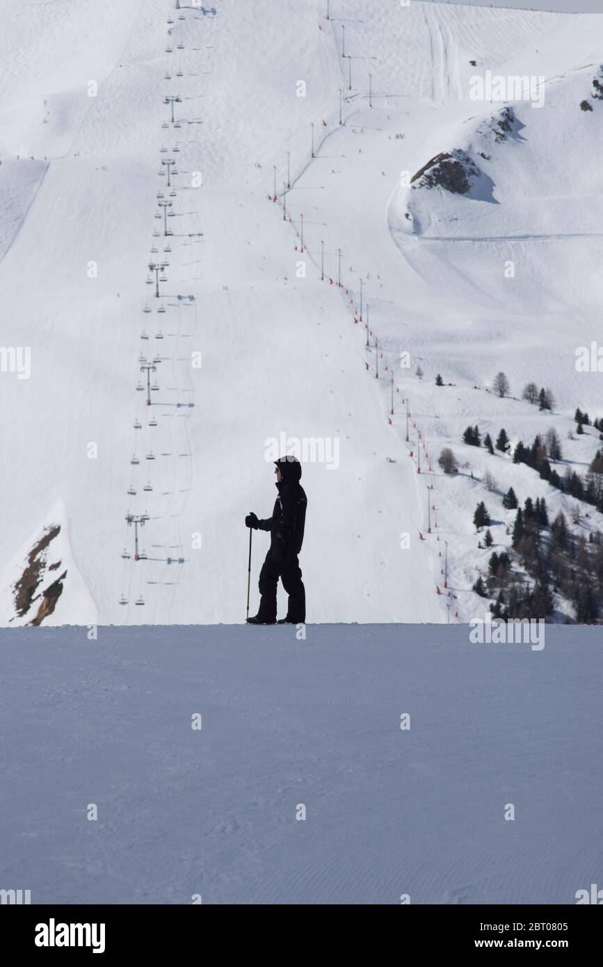 Woman skier standing in profile to a distant ski piste at La Plagne, Savoie France Stock Photo