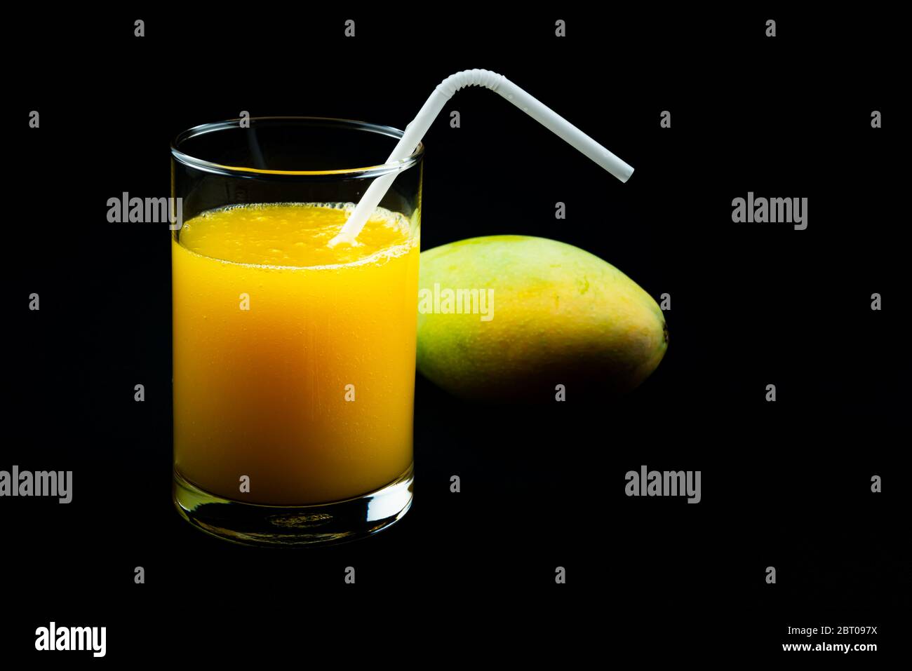 View of mango juice in a glass with a ripe mango on black background