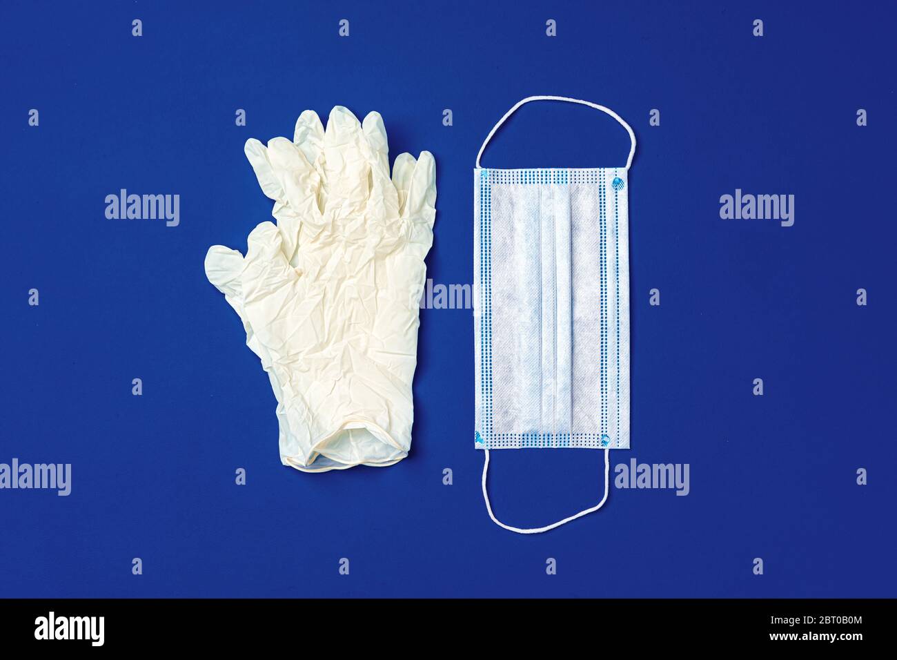 Medical gloves and surgical protective face mask on dark blue ...