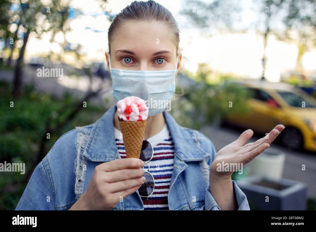 Woman in medical mask with ice cream in her hands on walk on street, close-up Stock Photo