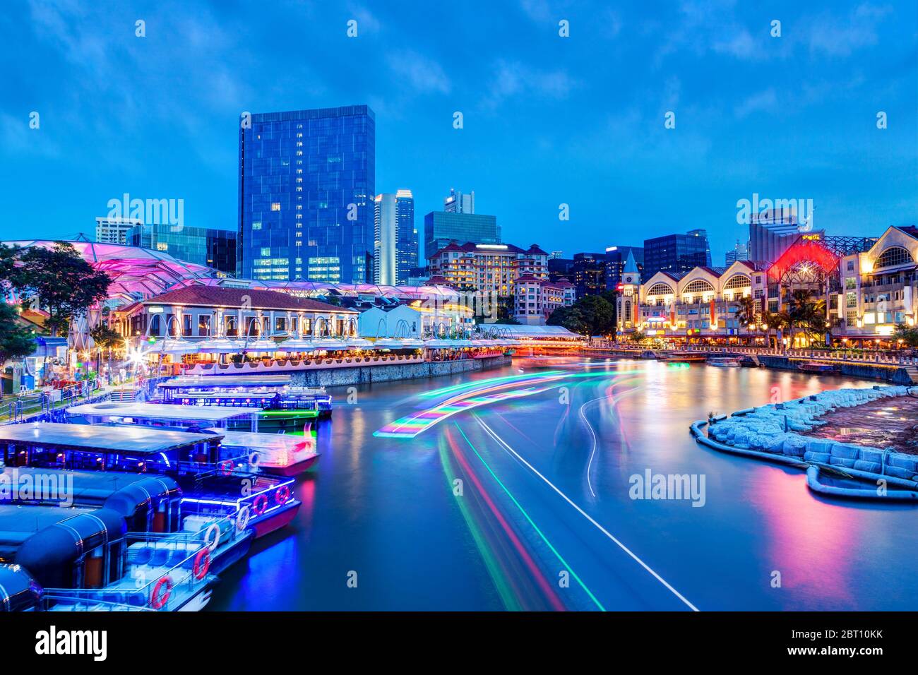 Sunset night life at Clarke Quay on Singapore River as colorful light trails from river boats and surrounding bars and restaurants light up the popula Stock Photo