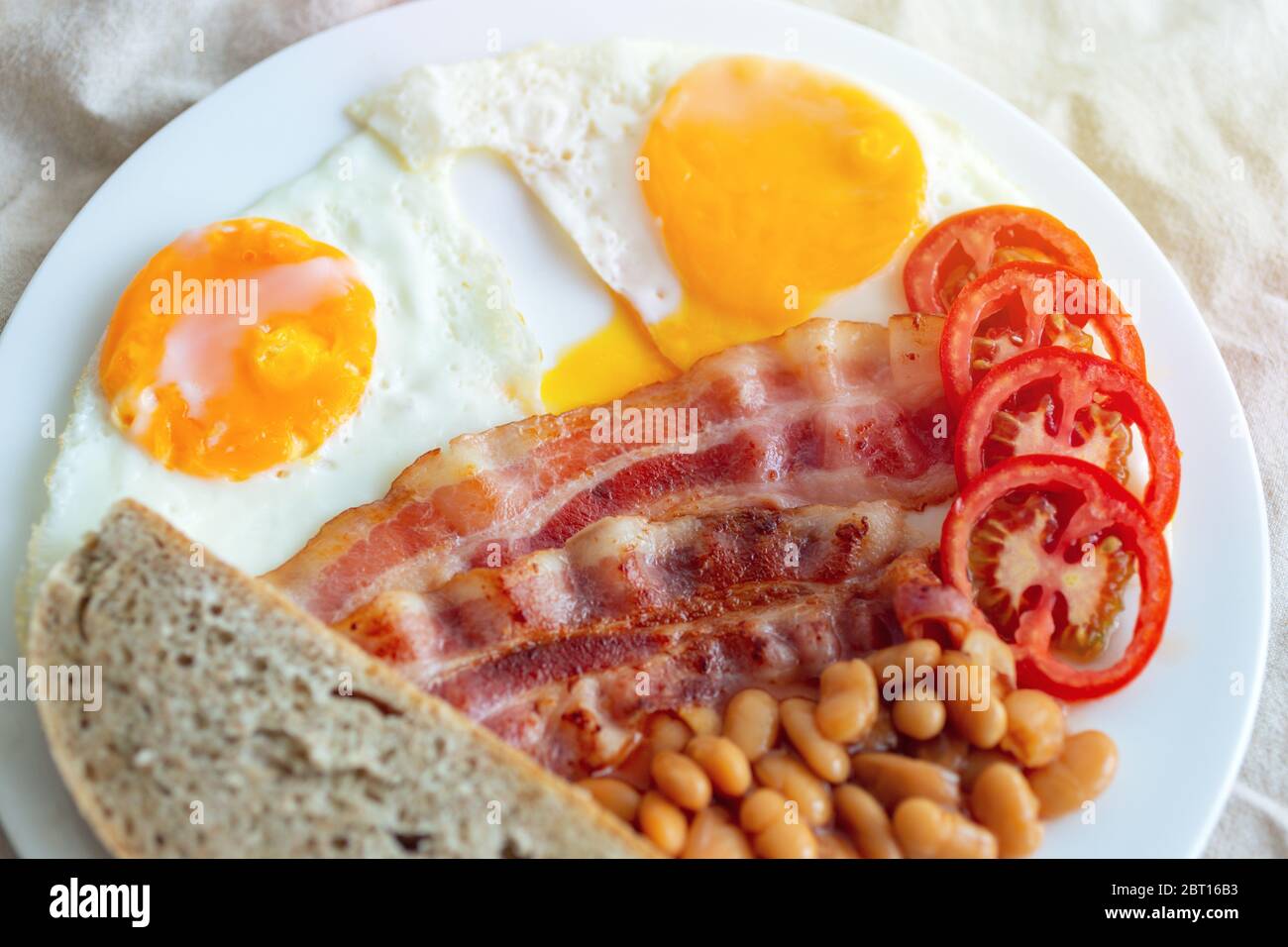 Close up of traditional English breakfast: fried eggs, bacon, beans, toast bread and tomato on a plate. Stock Photo