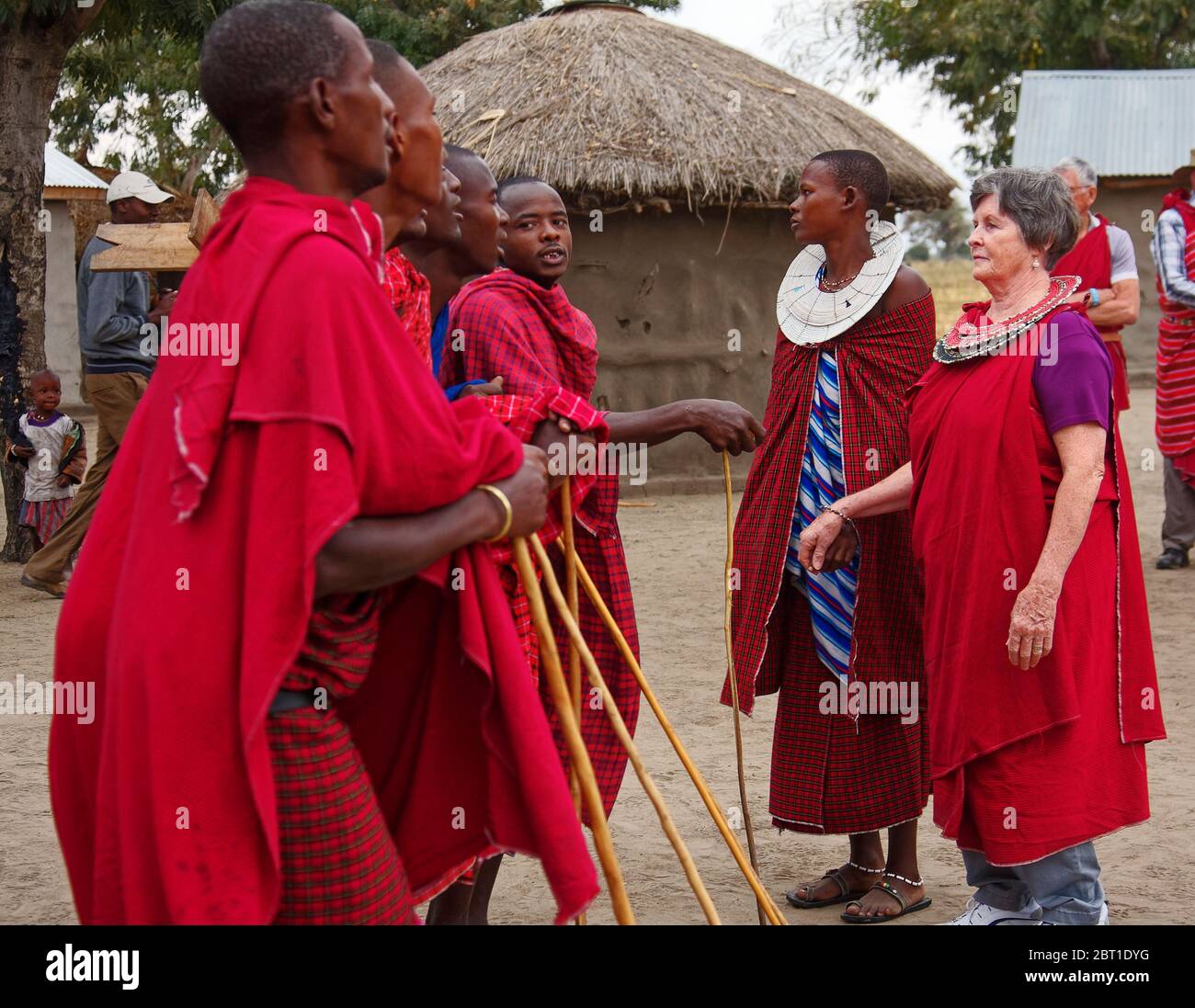 Maasai men, woman, female visitor, presenting to warriors, village; indigenous people; traditional red dress, beaded double collars, travel experience Stock Photo