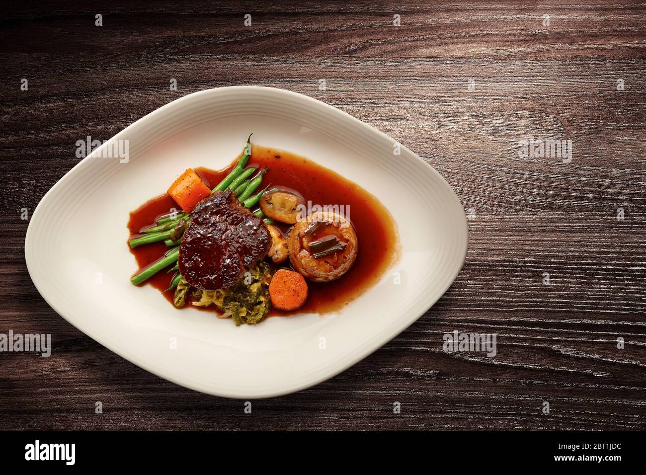 Directly above shot of a stylish Nouvelle Cuisine plate of beef and vegetables and gravy on wooden background Stock Photo