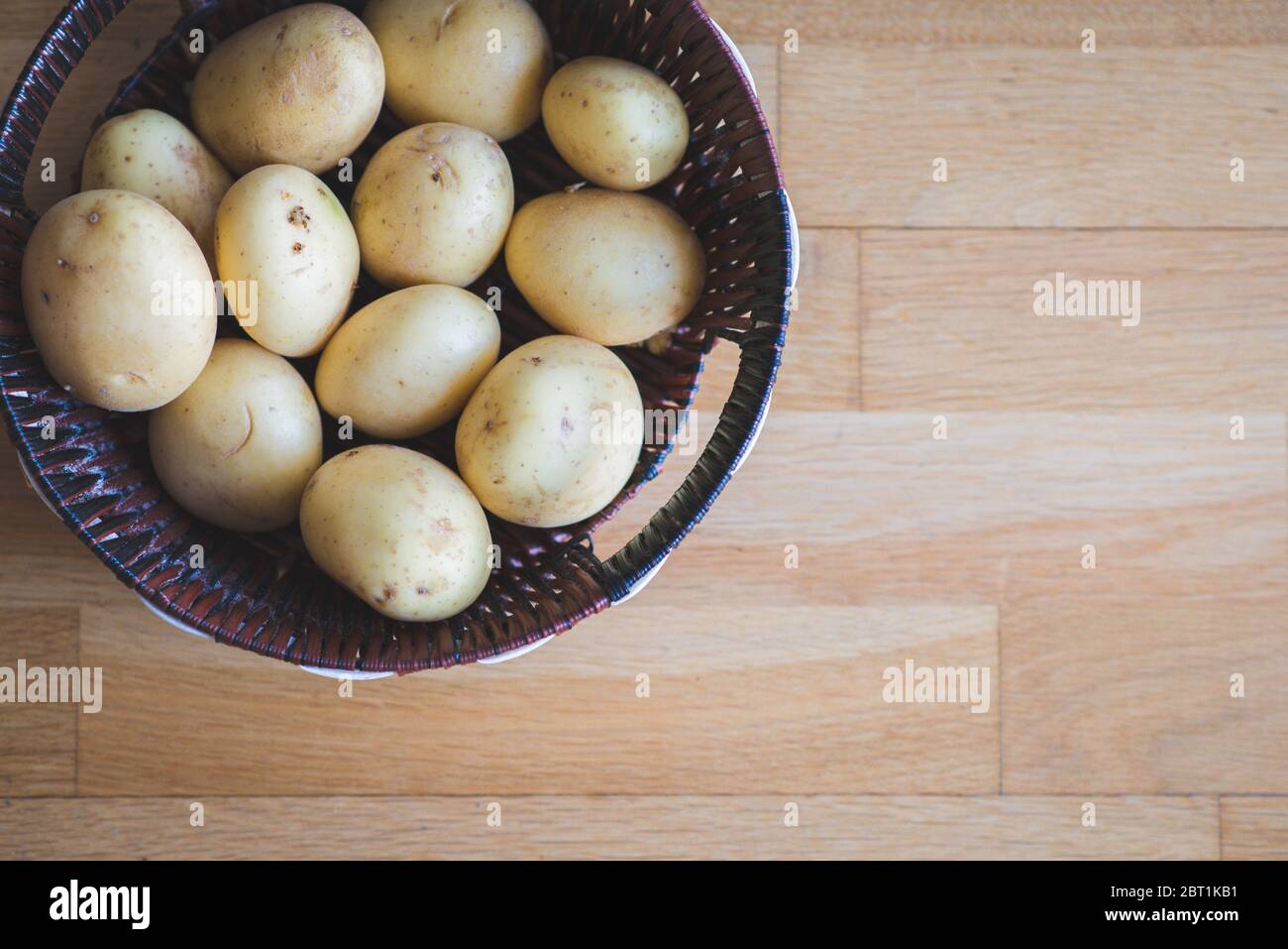 Potatoes in a wicker basket. Potato tubers in wicker dishes and scattered on the table. Potato harvest. Vegetables for a healthy diet. Stock Photo