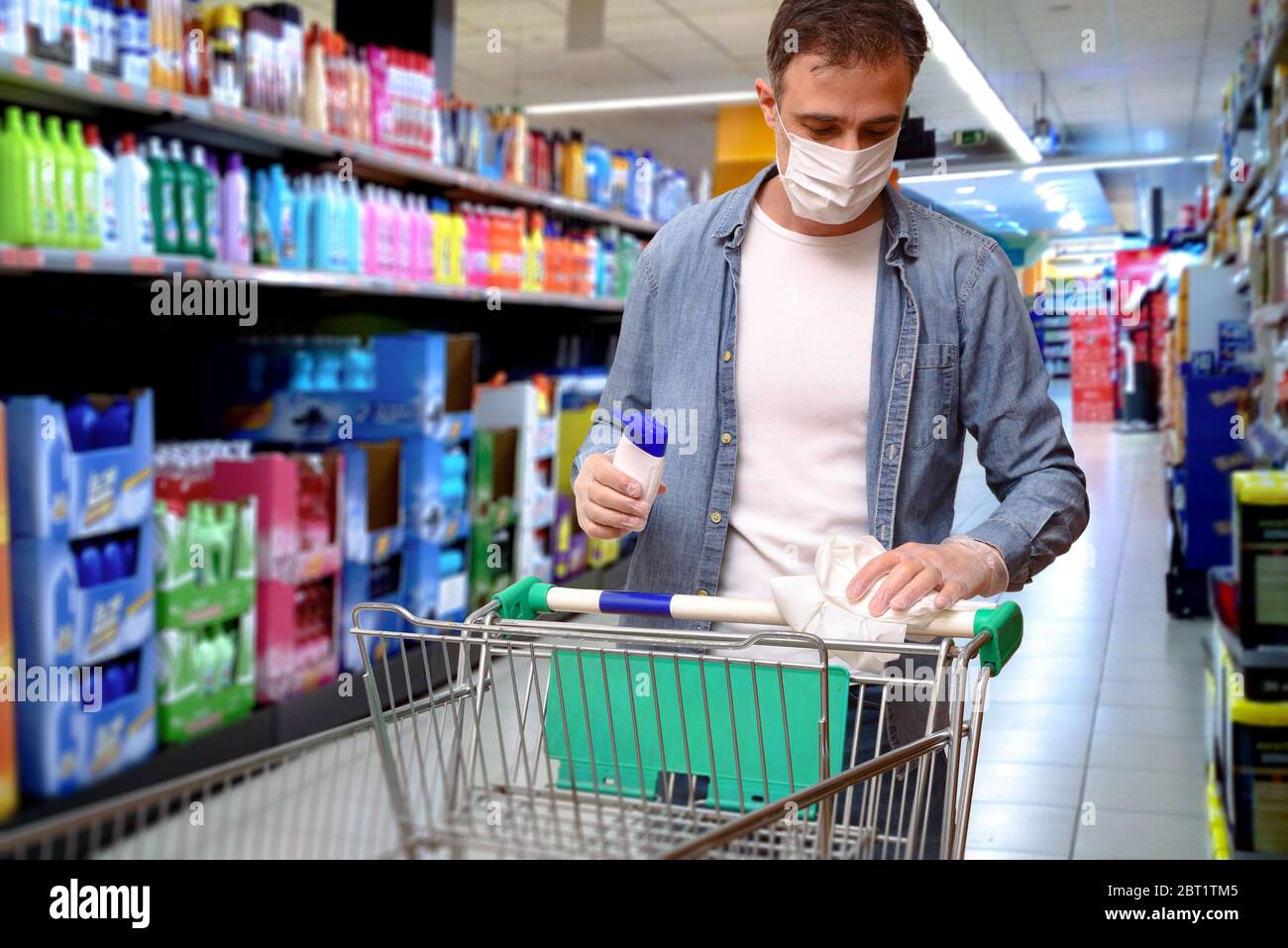 Supermarket consumer cleaning the shopping cart with disinfectant gel before buying protected with gloves and mask Stock Photo
