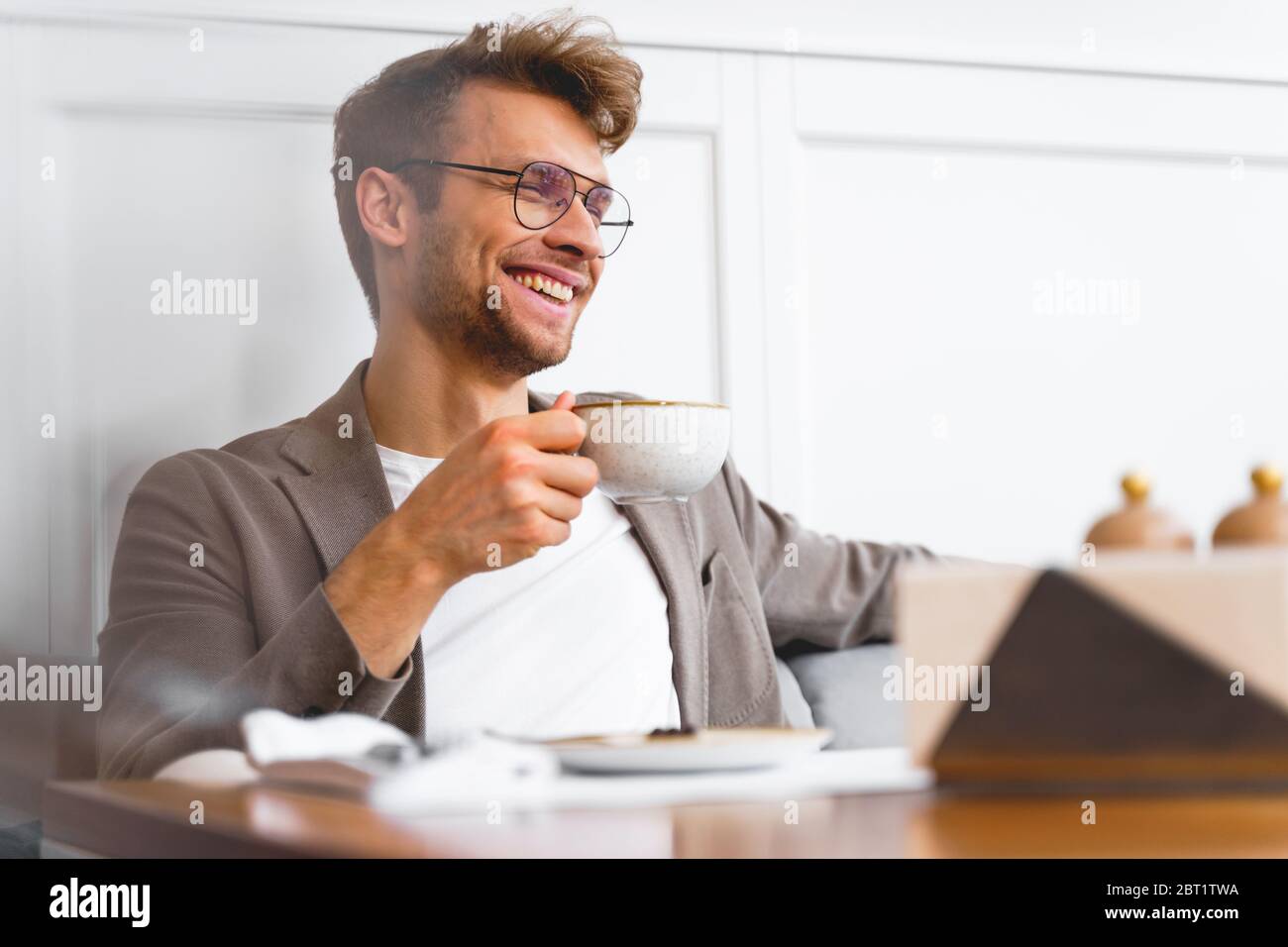 Cheerful young man drinking coffee in cafe Stock Photo