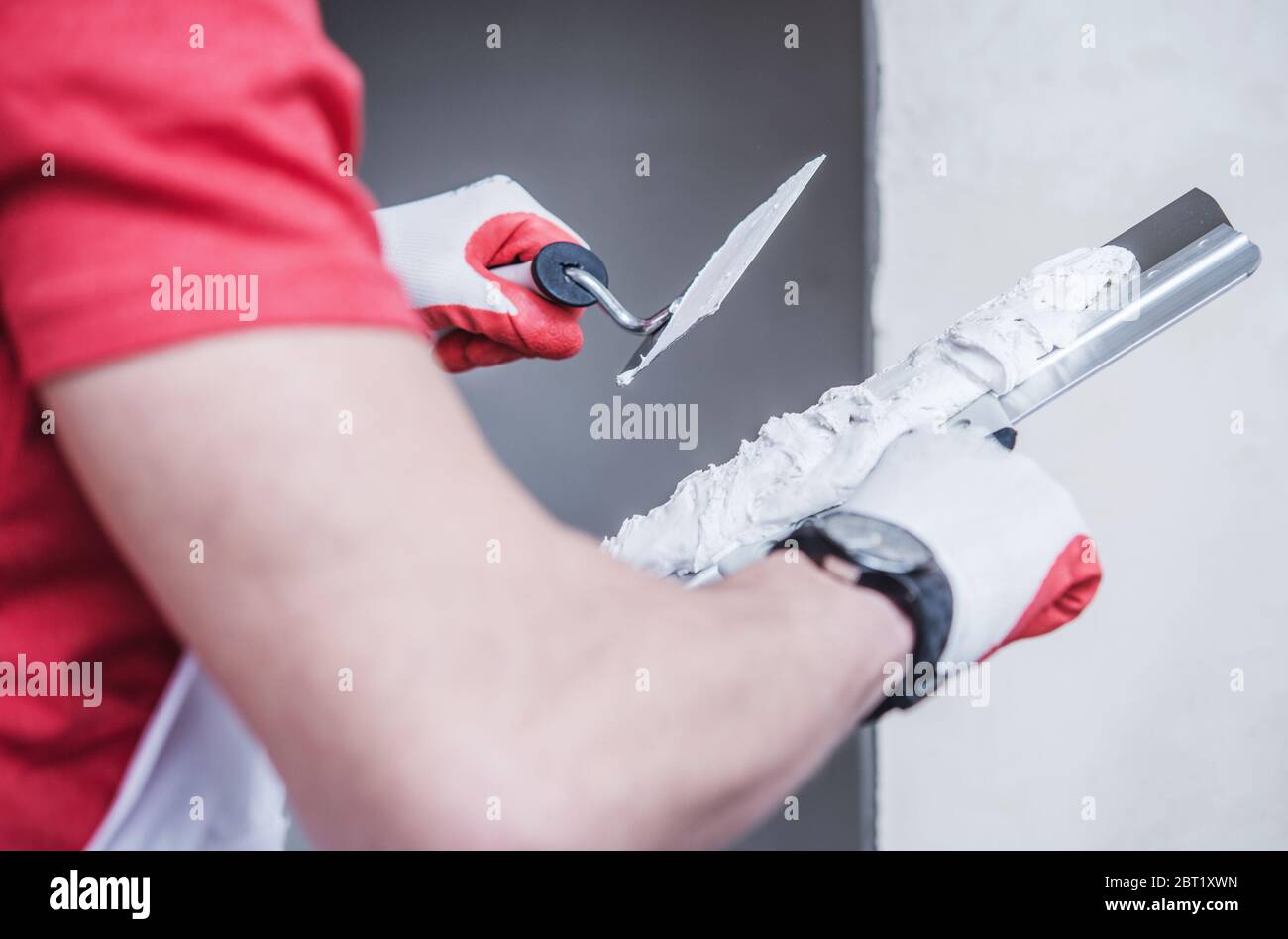 Close Up Of Construction Male Worker Applying Thin Coat Of Drywall Compound Using Professional Taping Knife. Stock Photo