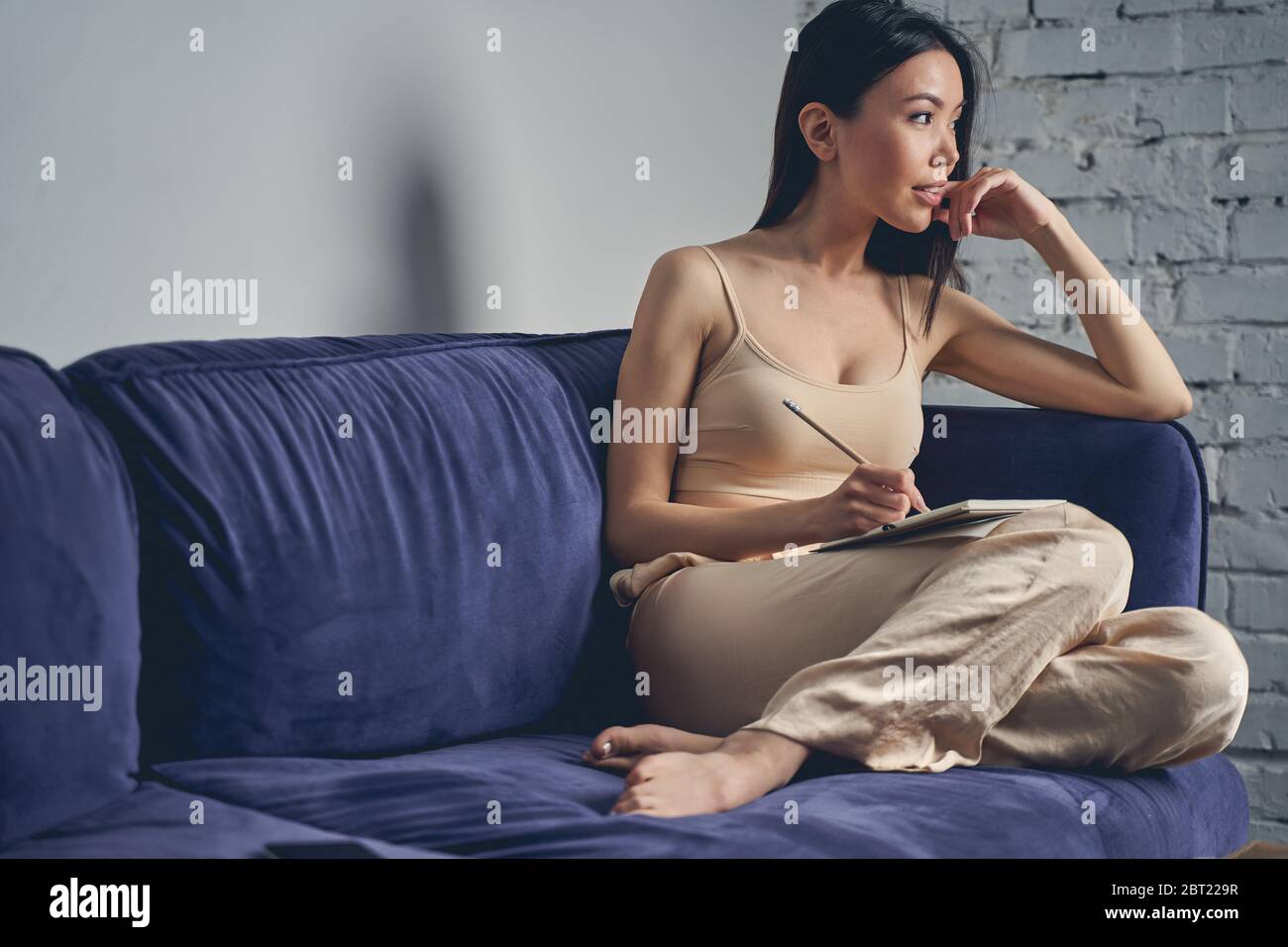 Beautiful young woman sitting on sofa at home Stock Photo - Alamy