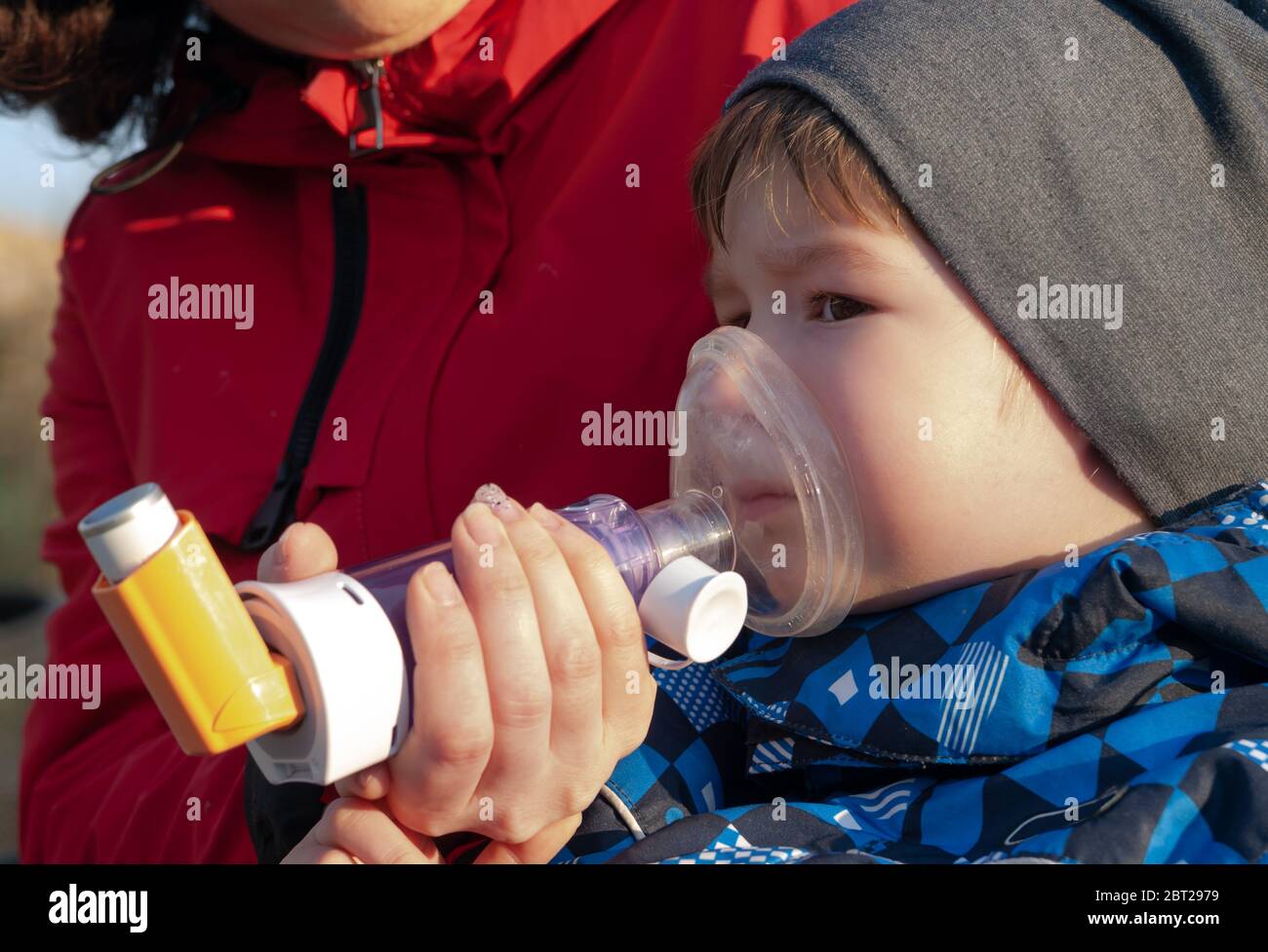 A small boy who suffering from illness bronchial asthma getting treatment with aerosol inhaler outdoors Stock Photo