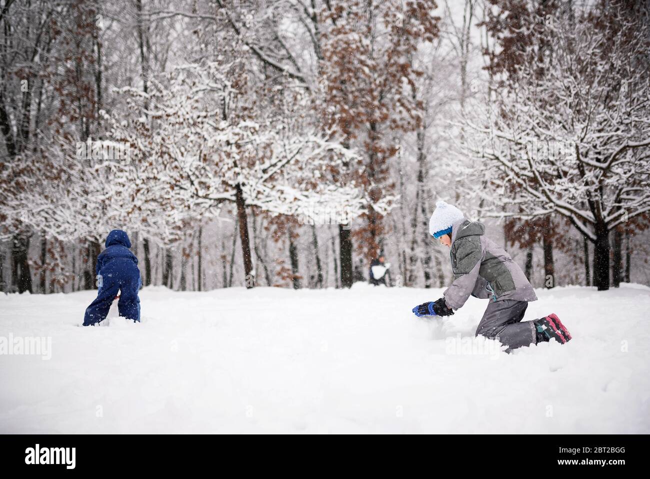 Two children rolling snow to make a snowman, USA Stock Photo
