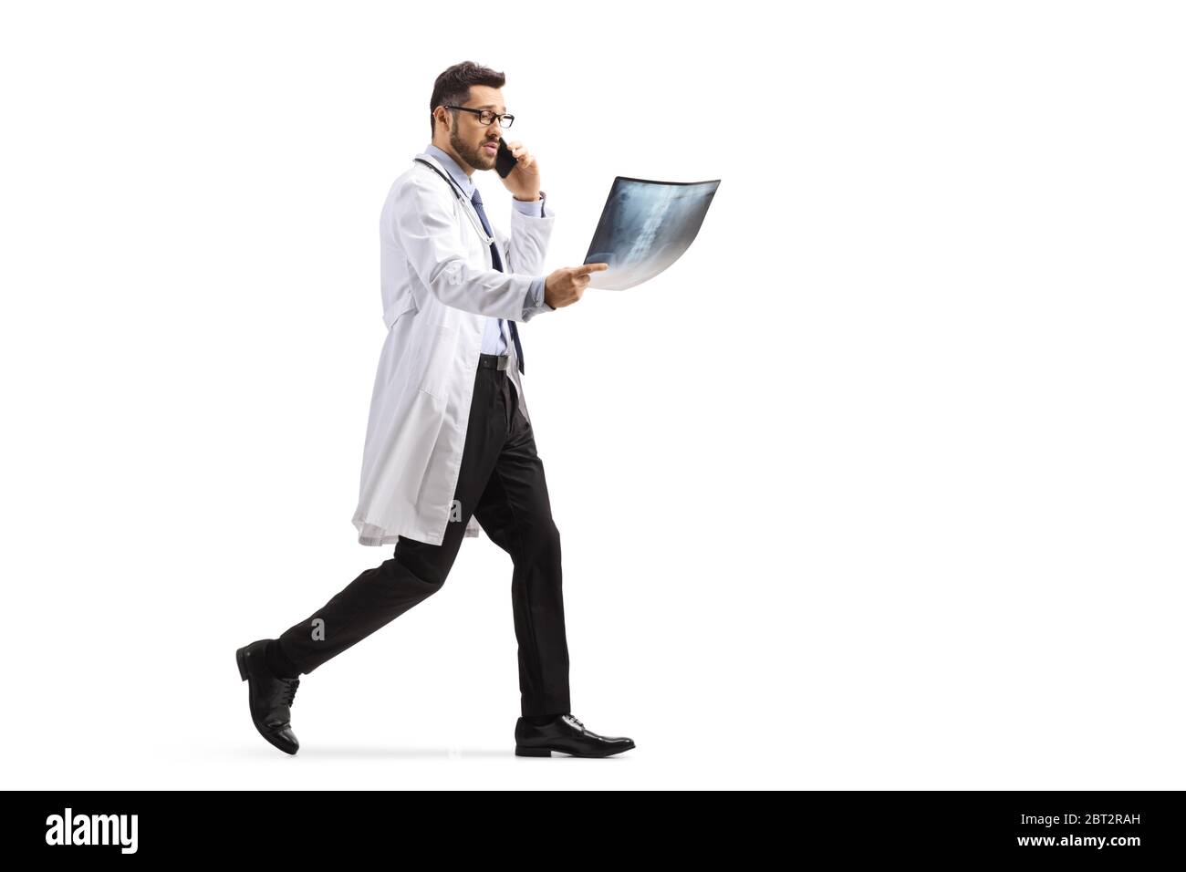 Full length shot of a male doctor walking with an x ray scan and talking on the phone isolated on white background Stock Photo