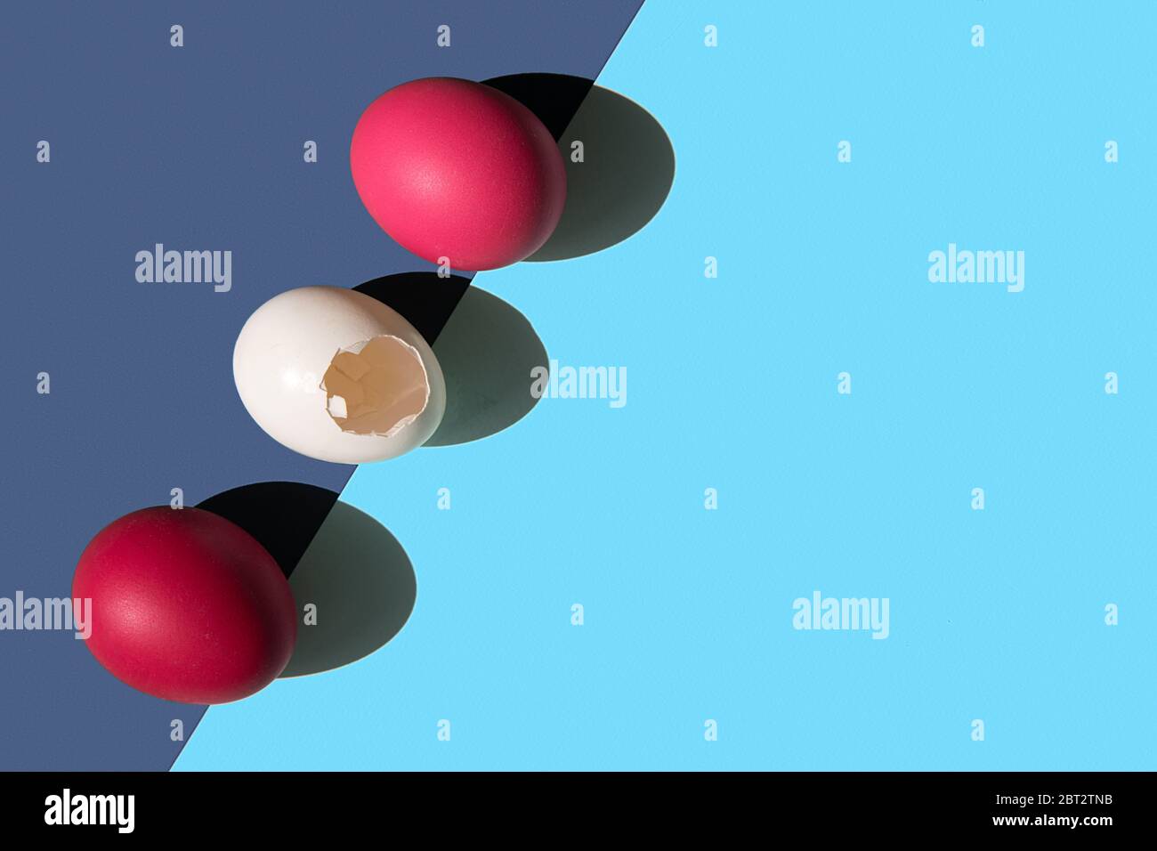 Three eggs are laid on the edge of the frame in a row. One egg is white. the shell of a white egg has a hole. Stock Photo