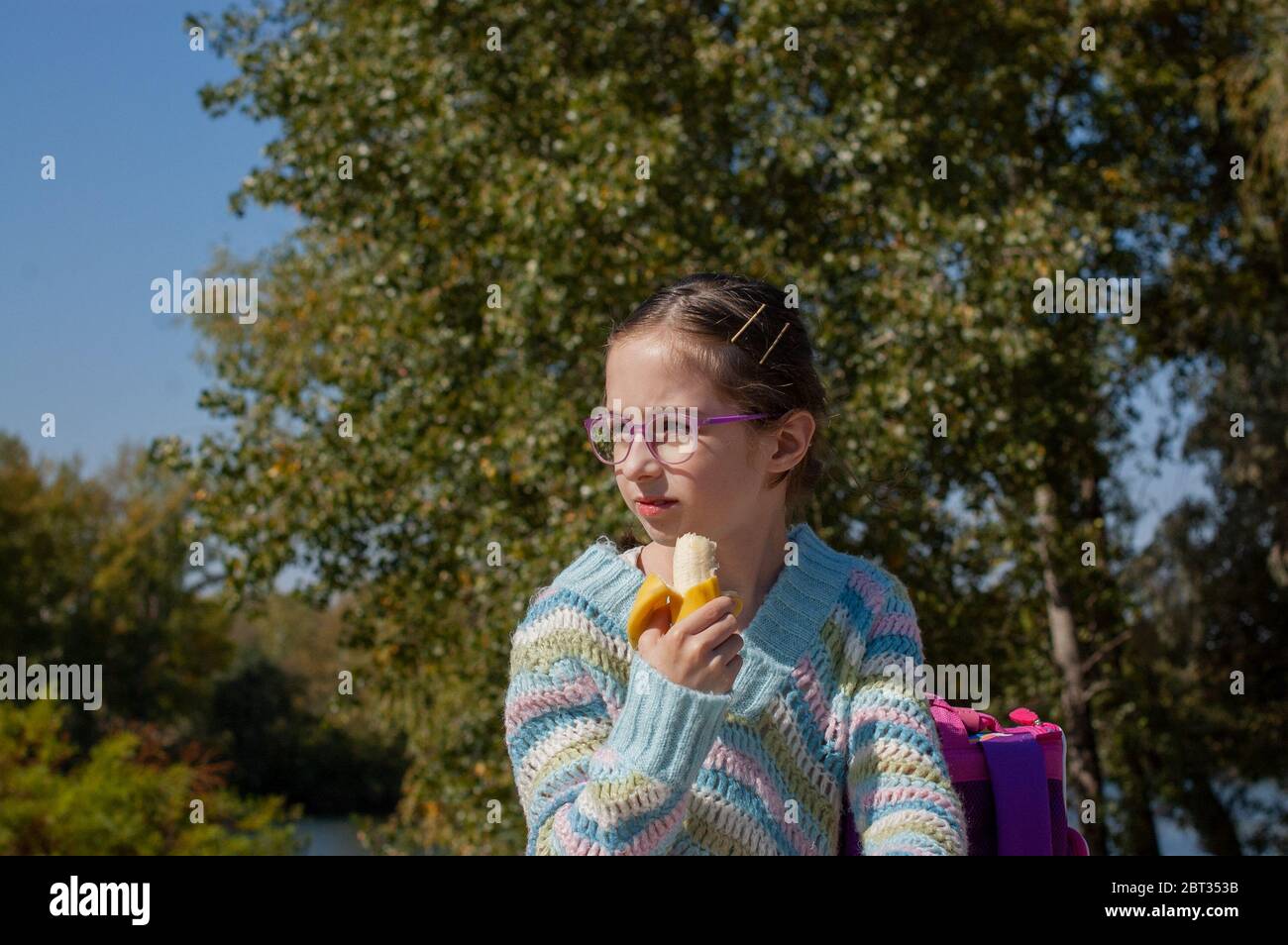 Schoolgirl eating a banana in the street. Alpha generation children will be the driving force behind progress in our century. They are more balanced, Stock Photo