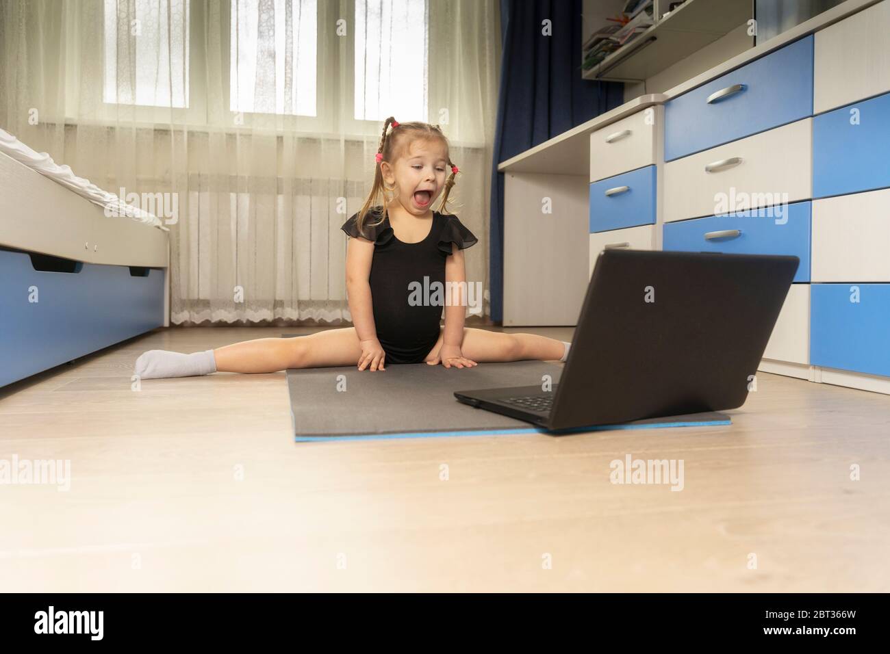 4 years old girl sitting on a twine in front of a laptop at home. online stretching exercises Stock Photo