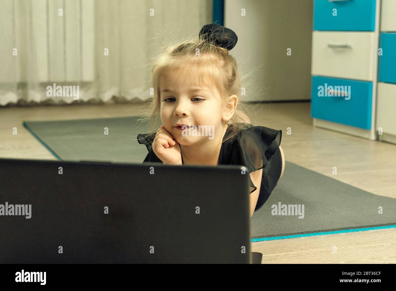 little girl in a gymnastics leotard lies on a gymnastic rug at home and is waiting for an online gymnastics lesson Stock Photo