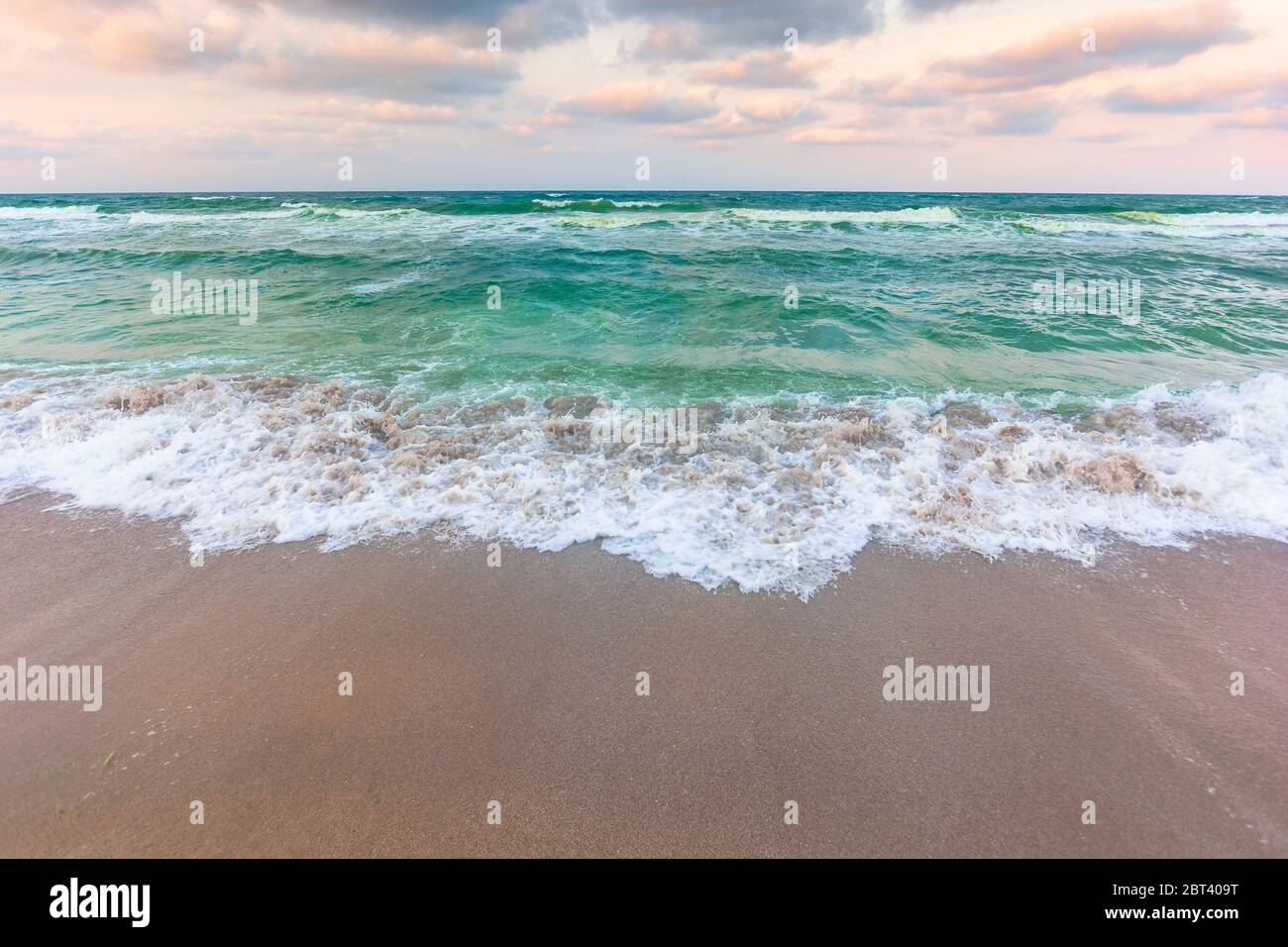 golden beach and green sea on a cloudy evening. beautiful view of waves rolling the coast beneath a glowing sky Stock Photo