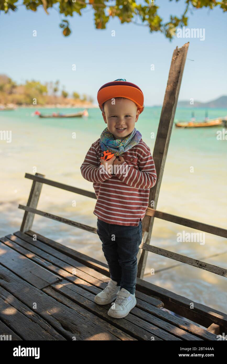 Fashion child. Happy boy model. Stylish little boy in baseball. Handsome kid. White Sneakers. red cap.Aquamarine sea background Stock Photo