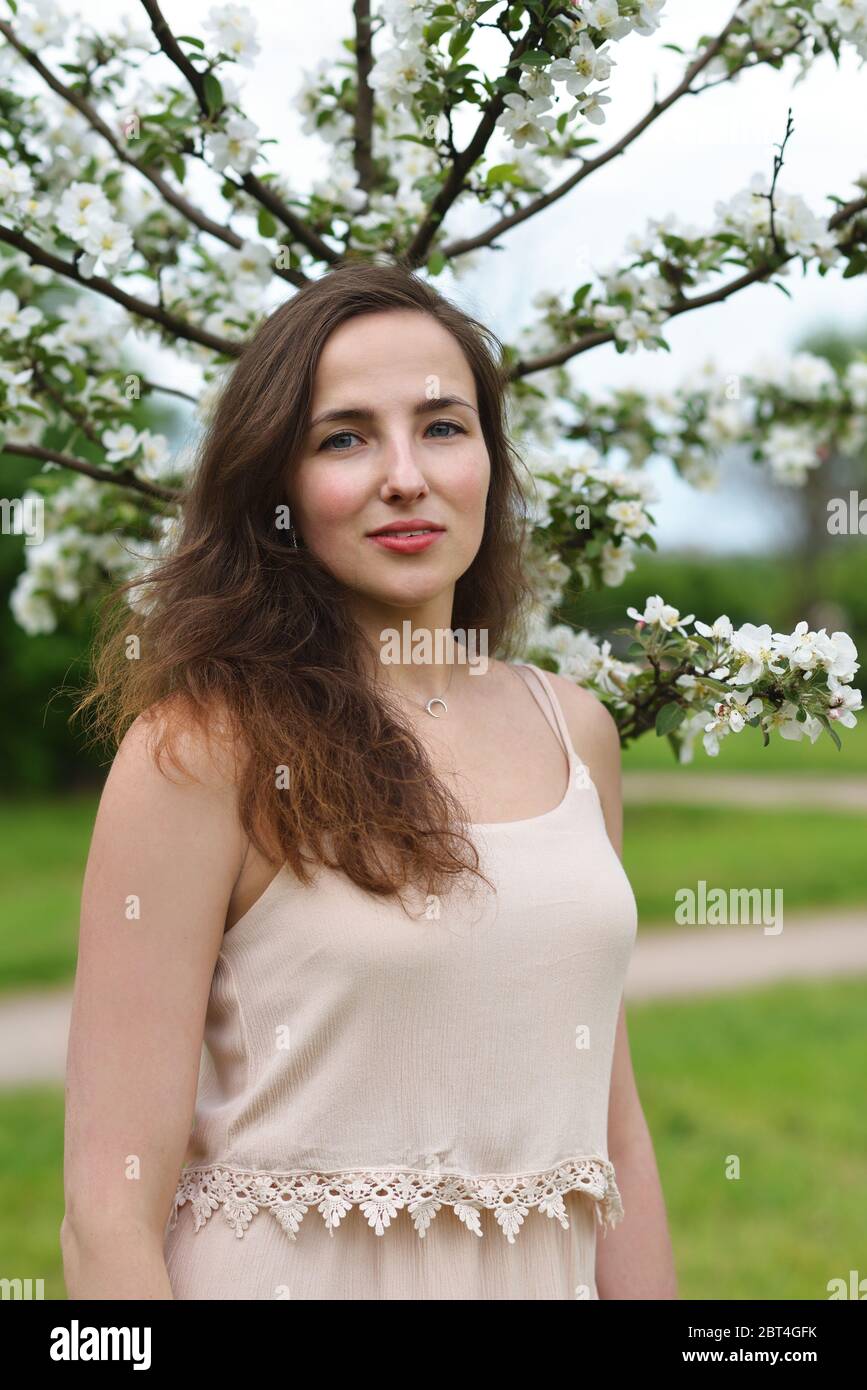 A beautiful girl stands against the background of a young blooming Apple tree Stock Photo