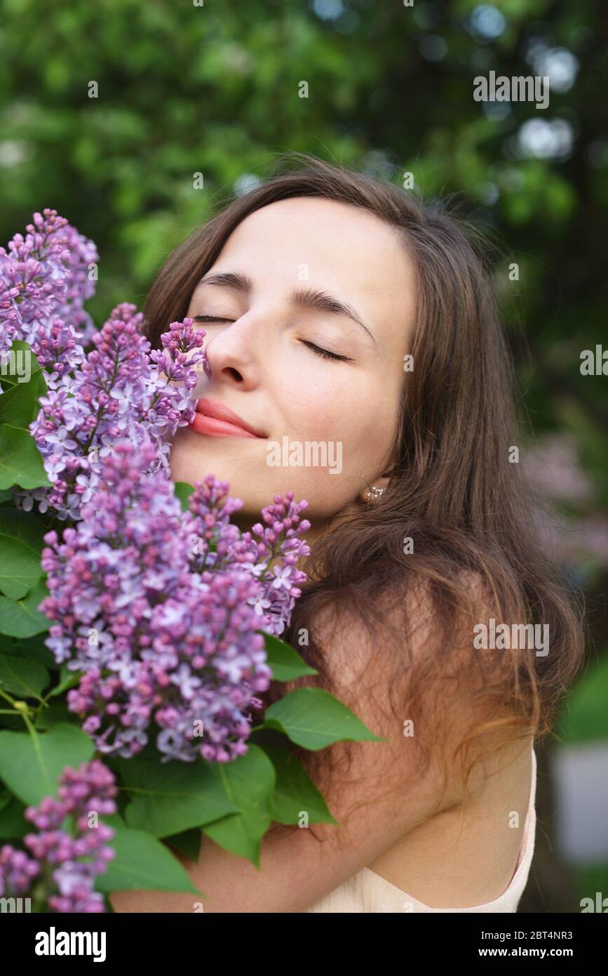 A young beautiful girl with closed eyes embraces a branch of blooming ...