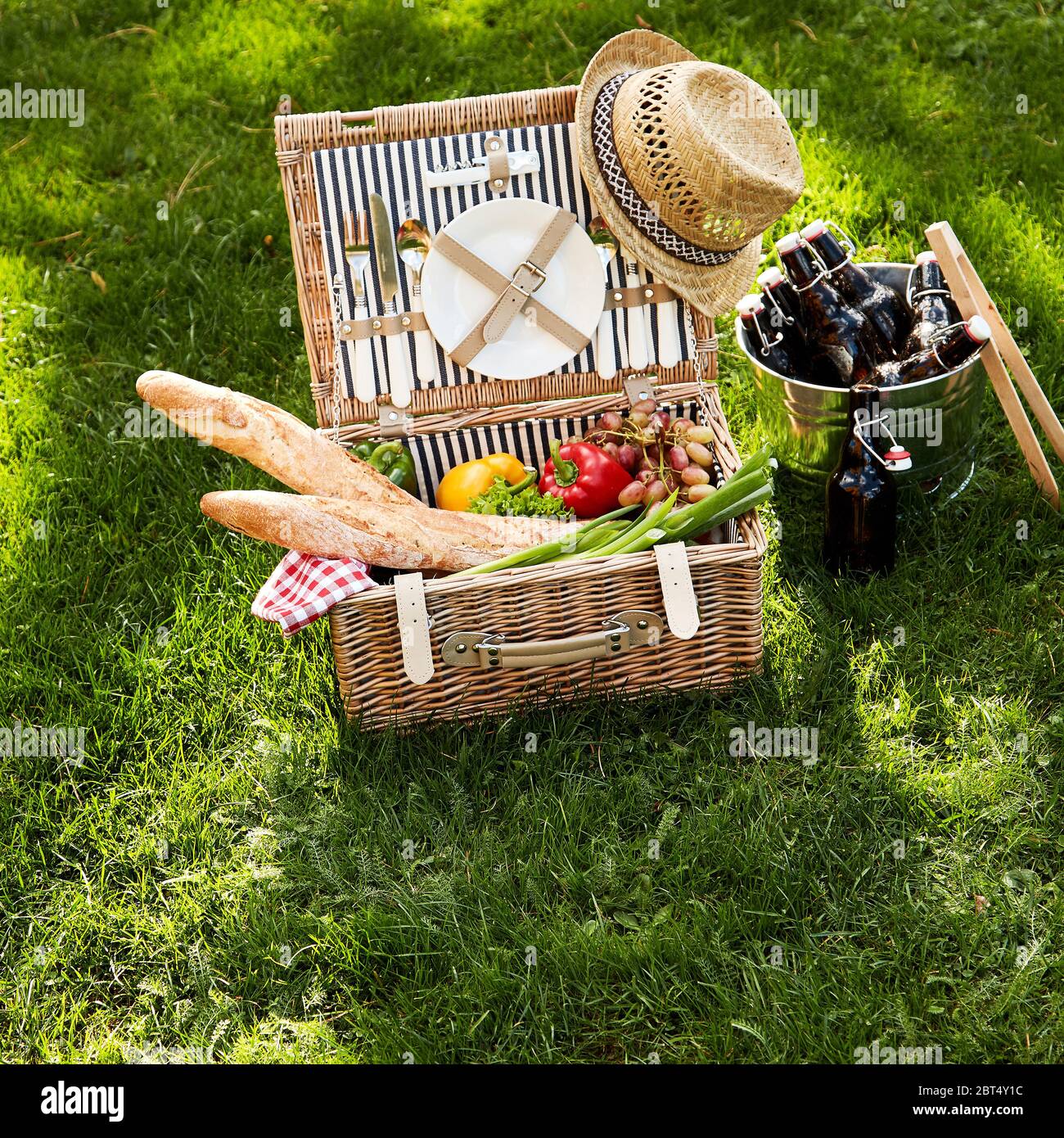 Healthy vegetarian summer picnic hamper with assorted fresh vegetables, French baguettes and grapes alongside a silver wine cooler filled with bottles Stock Photo