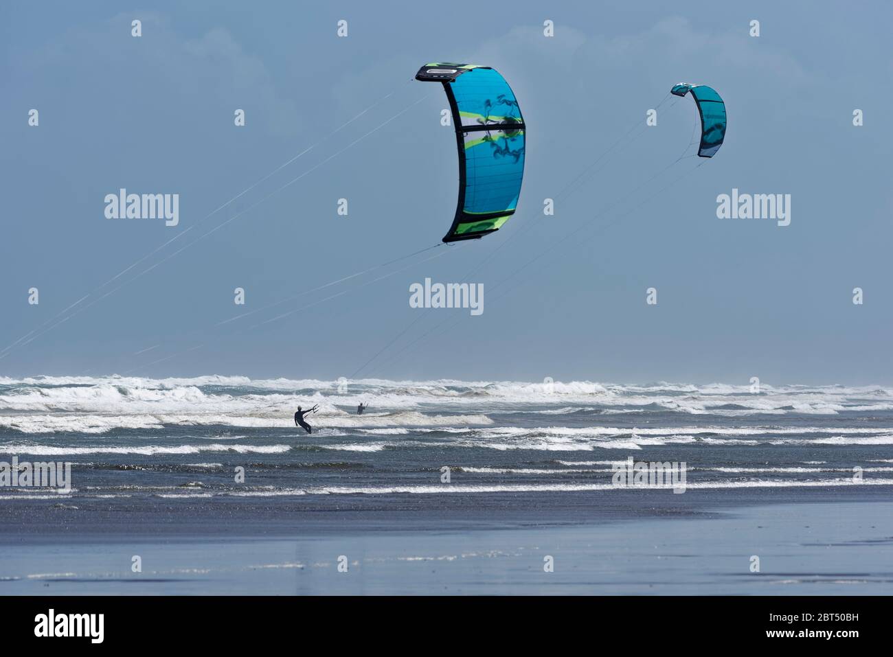 A couple of kite surfers amongst the waves near the shore on a windy day Stock Photo