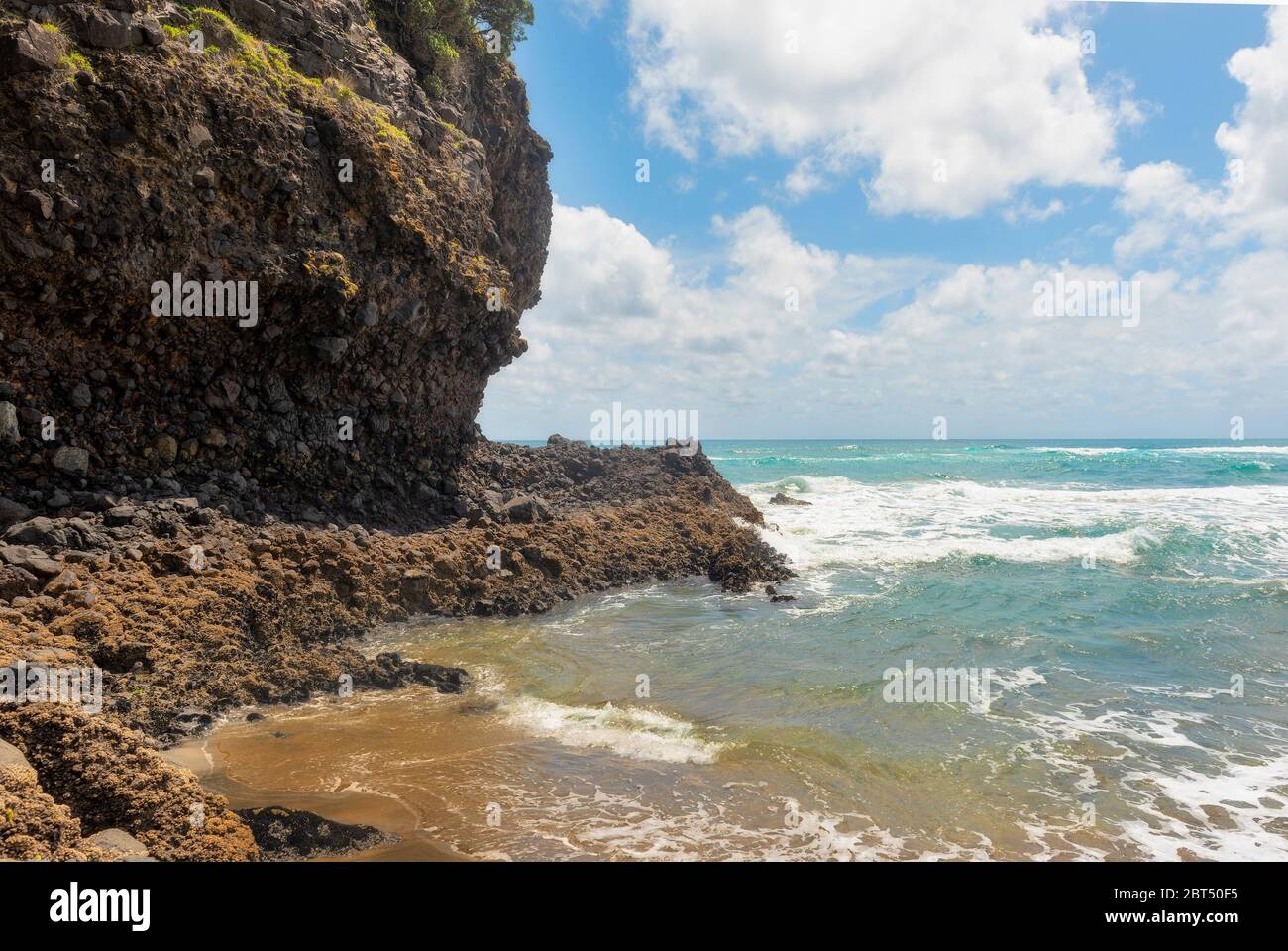 Waves pounding a rocky shore under blue cloudy skies Stock Photo