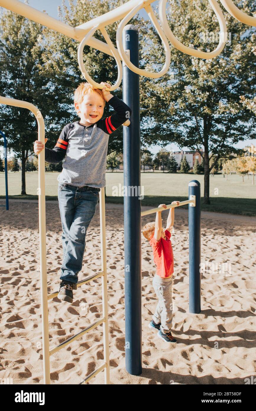 Young Caucasian boys friends hanging on monkey bars and pullup bars in