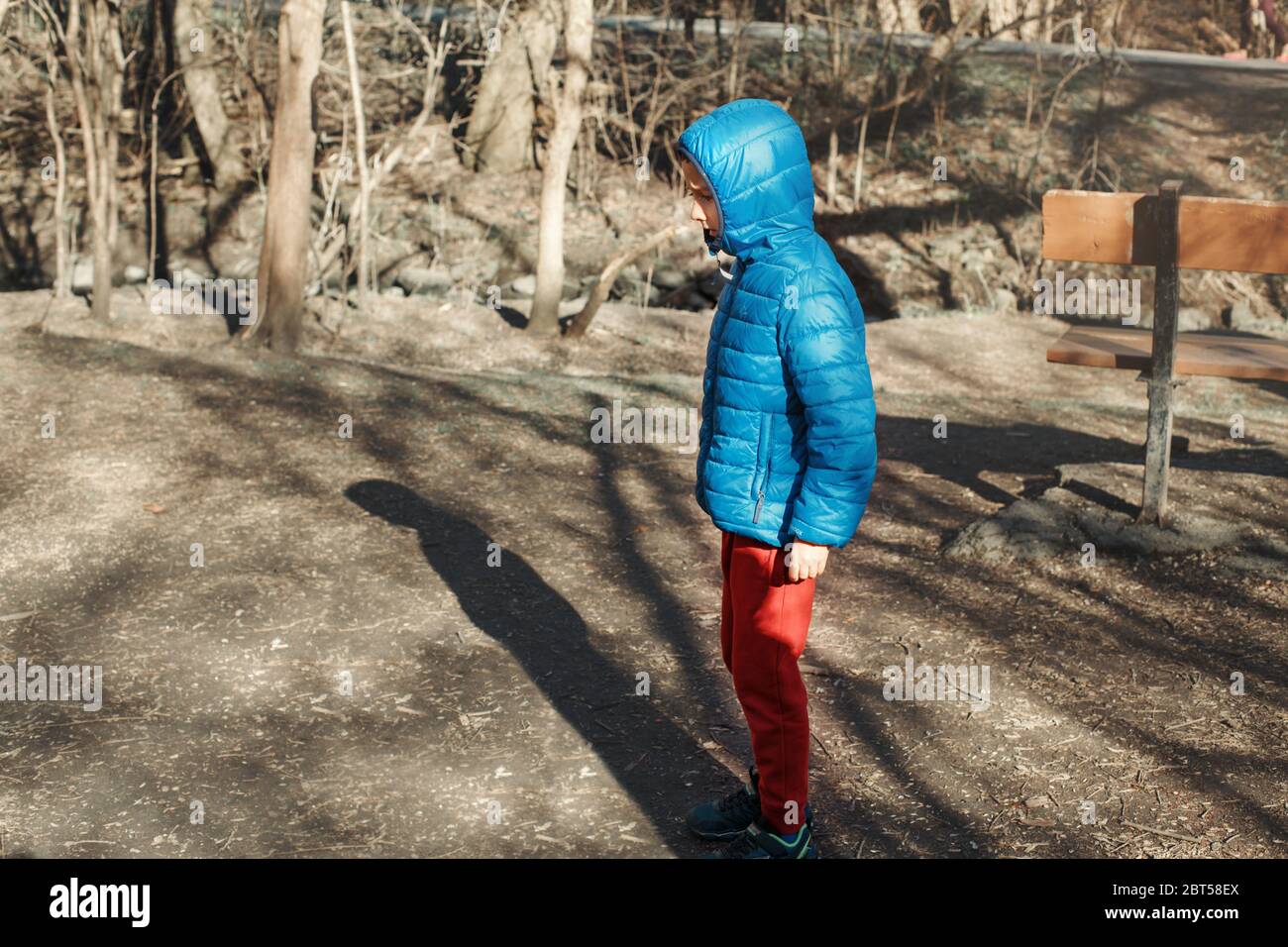Preschool Caucasian boy walking alone in park forest outdoor. Lost kid alone looks worry concerned. Child standing in street outside looking for Stock Photo