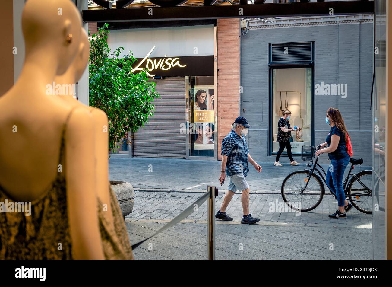 Seville, Spain; May 22, 2020: Blurry people (fast motion) walking on a commercial street after lockdown. Selective focus on the wall on the background Stock Photo