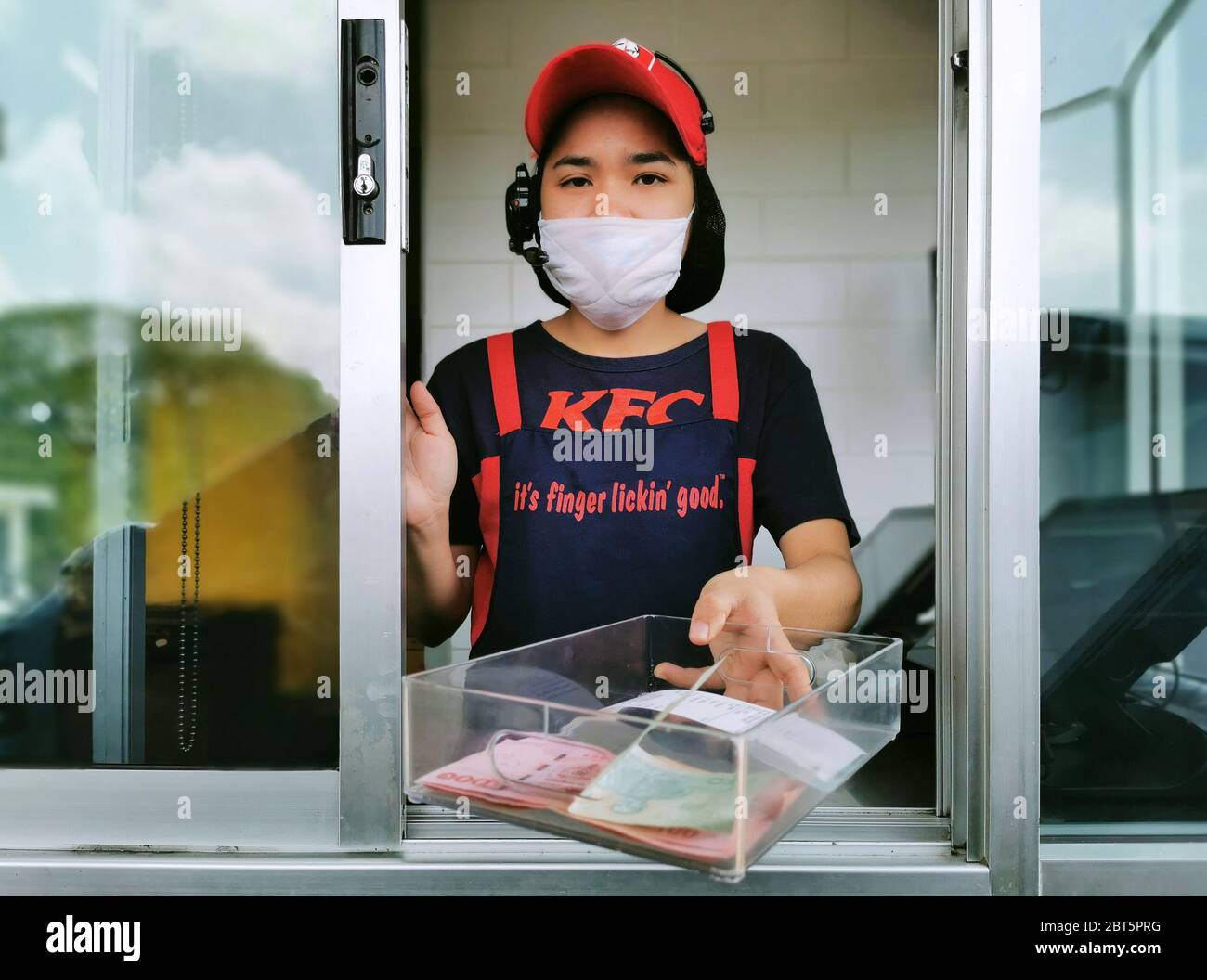 Bangkok, Thailand - May 7, 2020 : KFC fast food cashier in drive thru service waring hygiene face mask to protect coronavirus pandemic or covid-19. Stock Photo