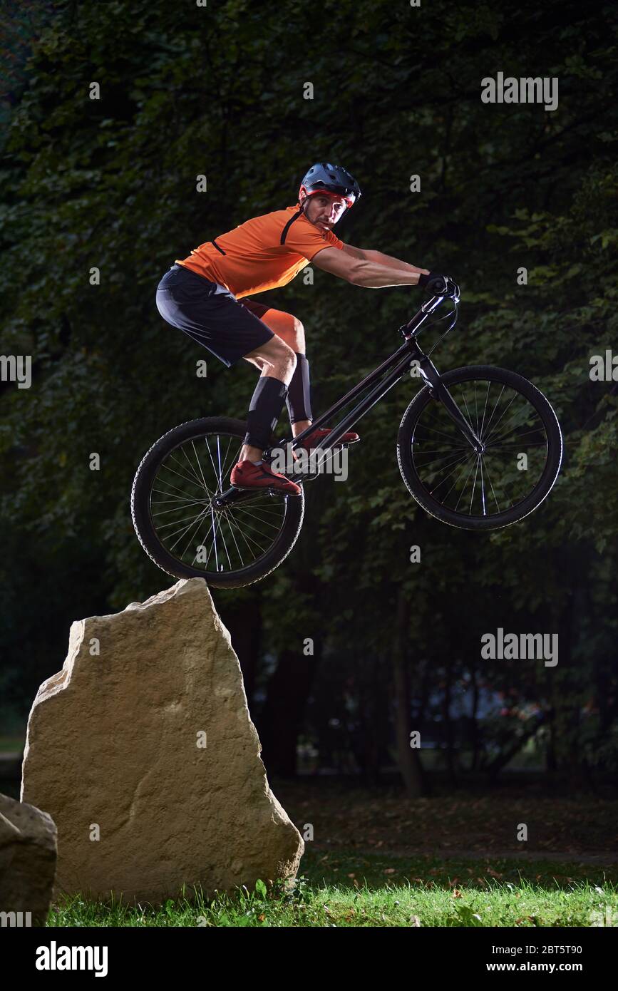 Front view of cyclist looking into camera during a high jump on a bicycle. Athlete keeping balance on back wheel of mountain sports bike. Concept of active lifestyle. Stock Photo