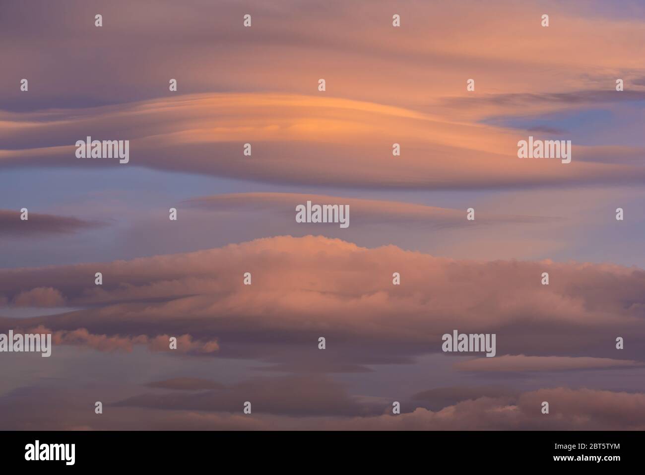 Lenticular clouds over the sky at dawn with reddish and orange colors Stock Photo