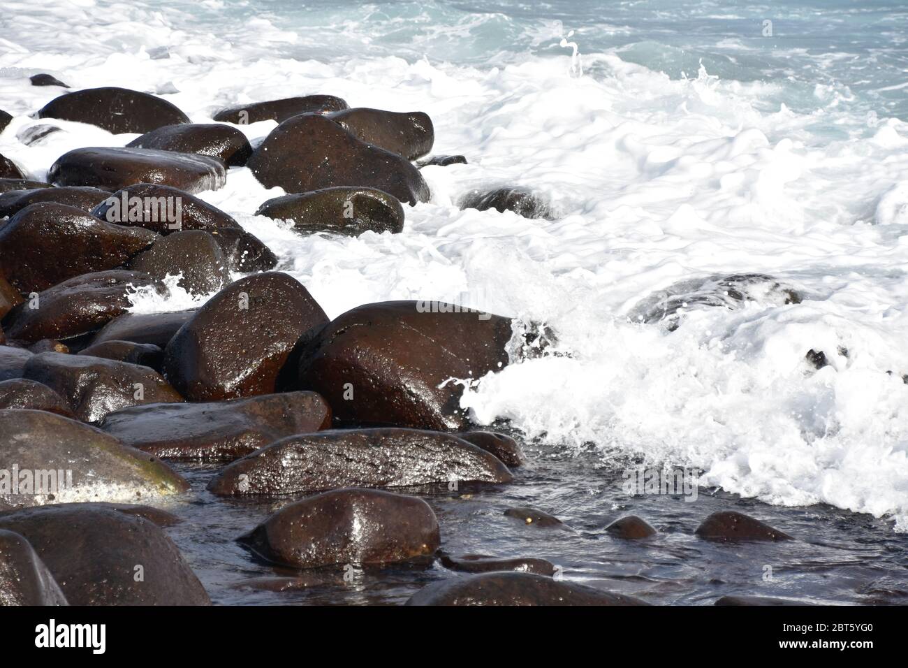 Waves break on stony rocky beach seashore Stock Photo