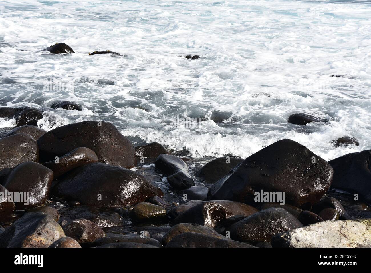 Waves break on stony rocky beach seashore Stock Photo