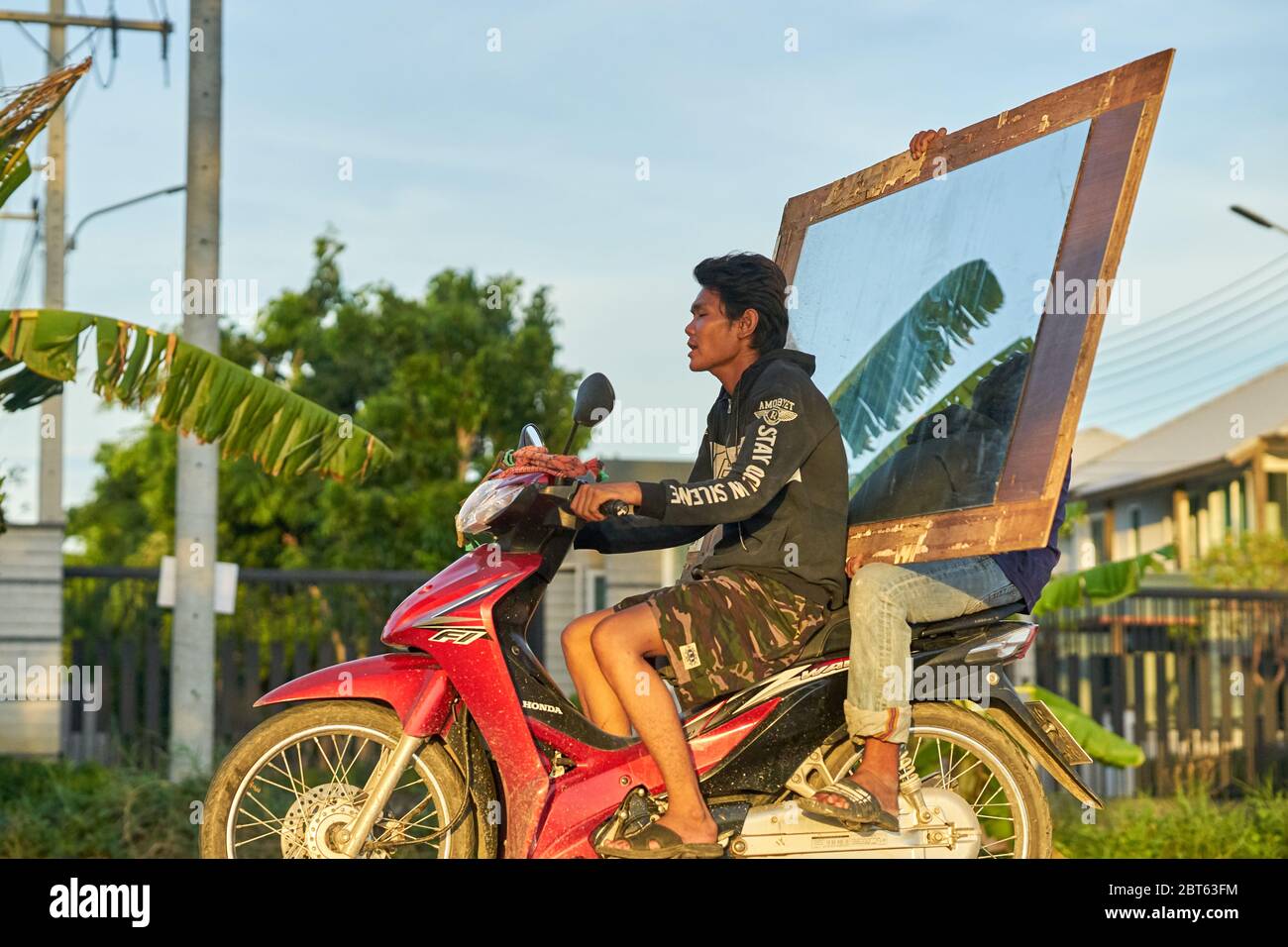 Two men on a scooter carrying a large mirror. Stock Photo