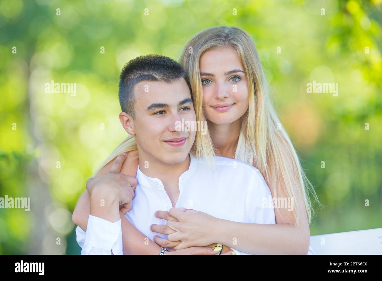 Beautiful young girl hugging her dark-haired boyfriend from behind ...