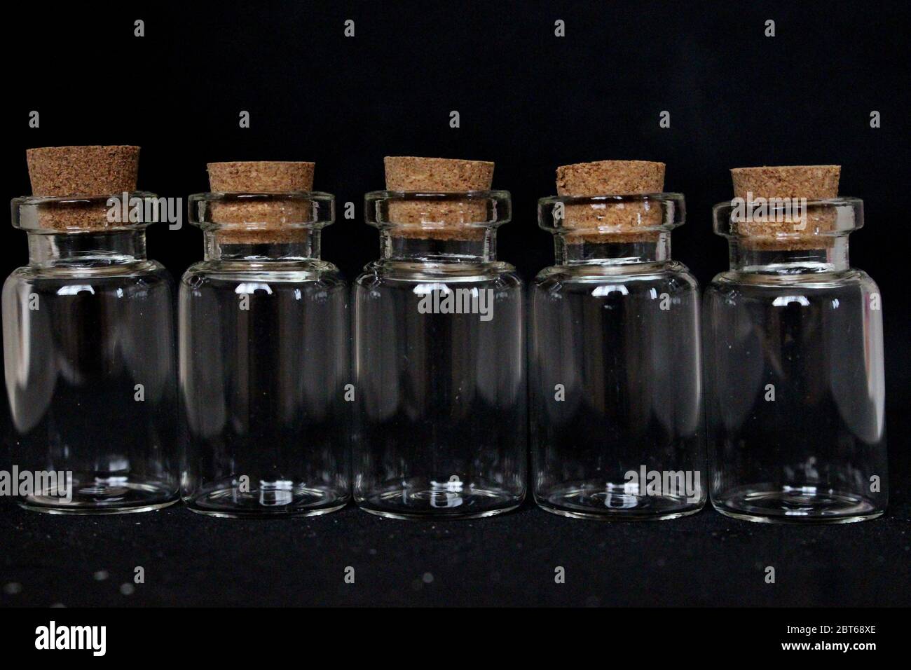A close up photograph of five empty glass bottles with cork stoppers, against a black background Stock Photo