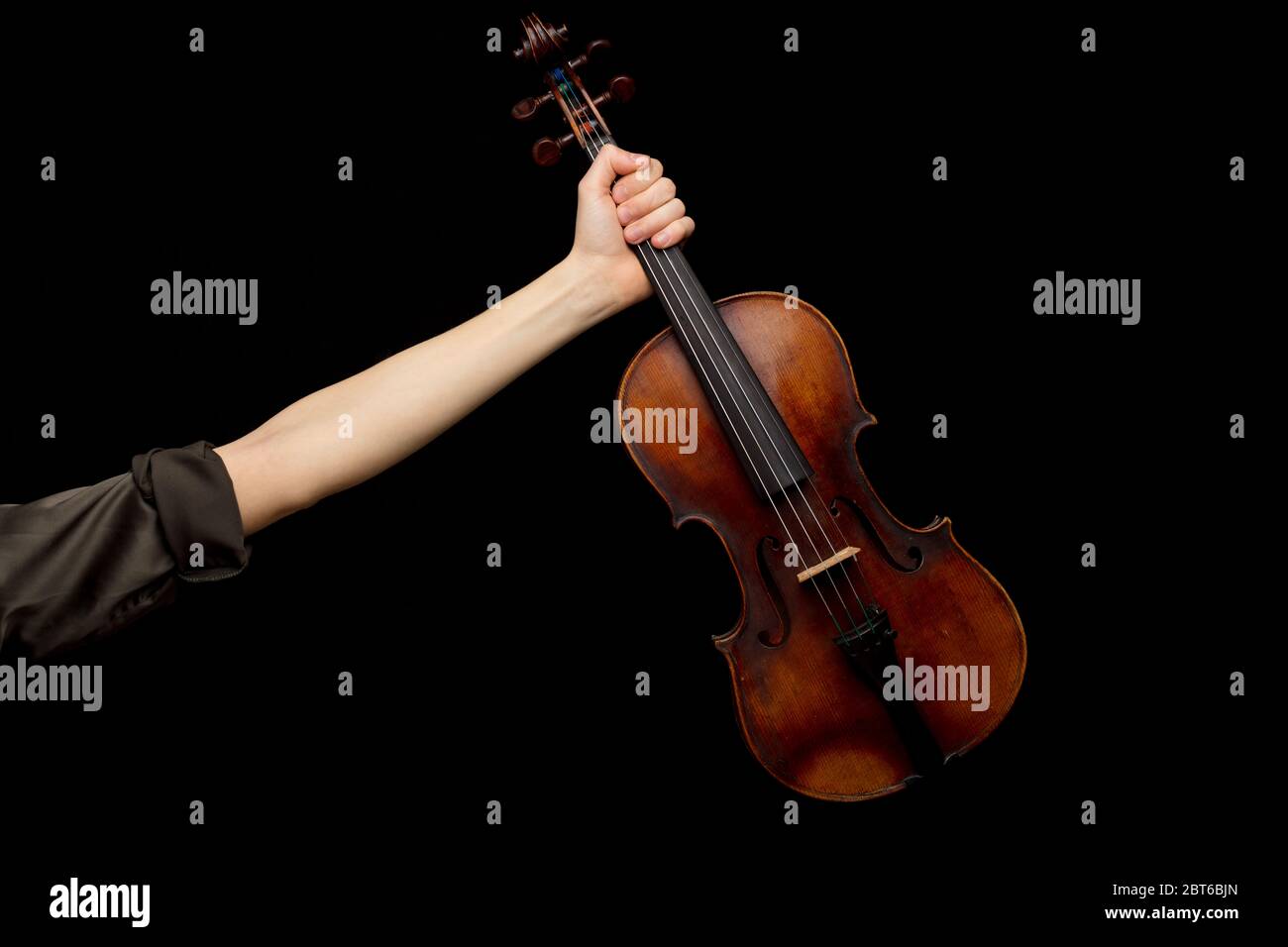 Woman displaying a classical baroque violin in her outstretched hand over a dark background with copy space set up in the original historic style Stock Photo