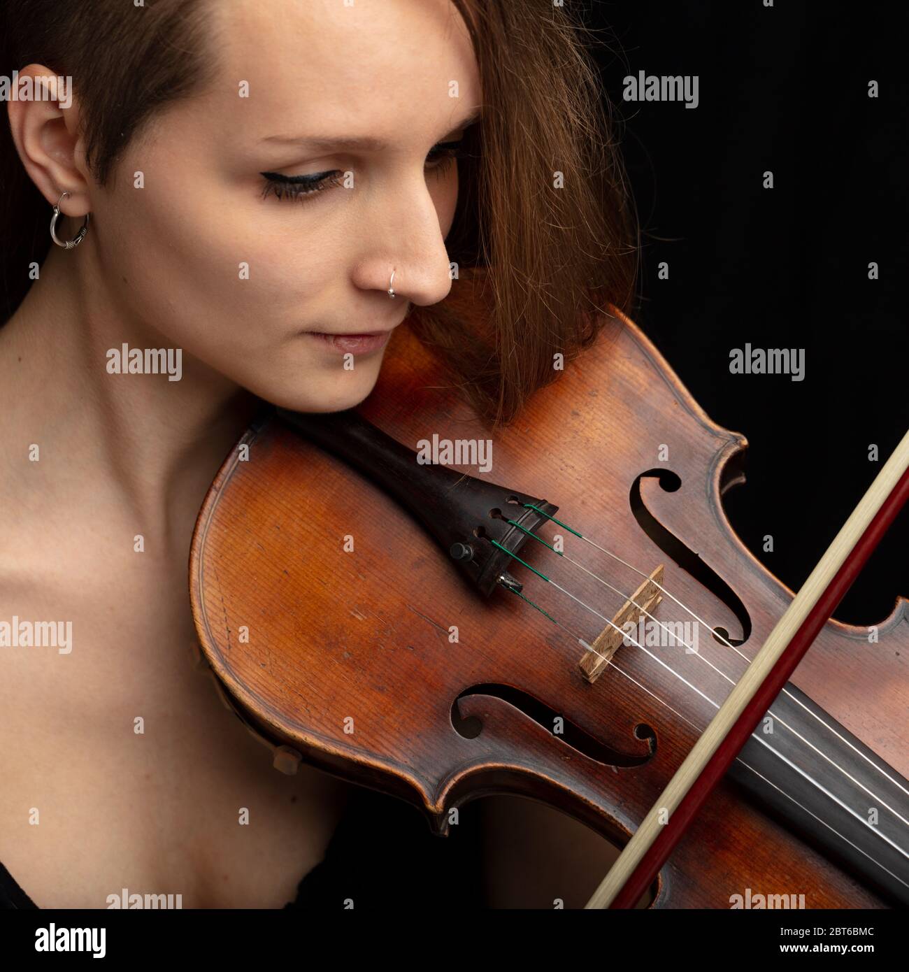 Woman with pierced nose playing a classical violin during a live performance or recital in close up on her face and instrument Stock Photo