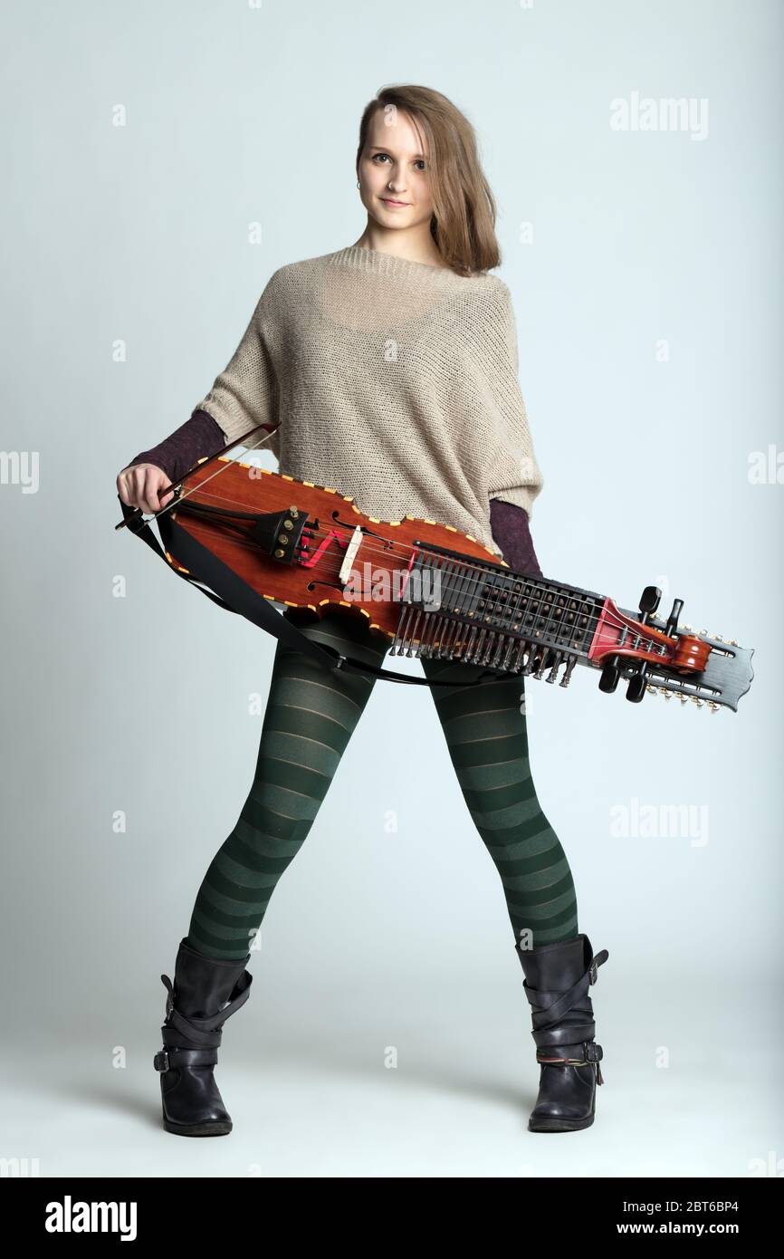 Trendy young woman musician with modern hairstyle wearing tights holding a modern reconstruction of a medieval Swedish nyckelharpa over white Stock Photo